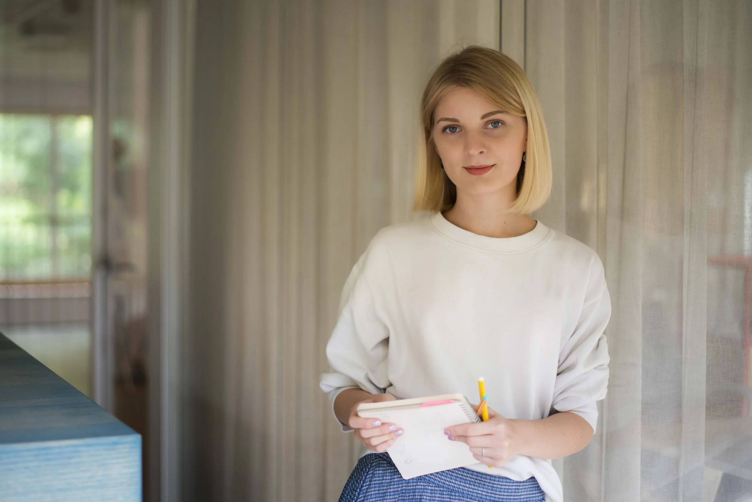 Žena stojící v moderním interiéru s blokem a tužkou v ruce, připravená zapisovat poznámky nebo prezentovat své nápady, firemní brand portrét.