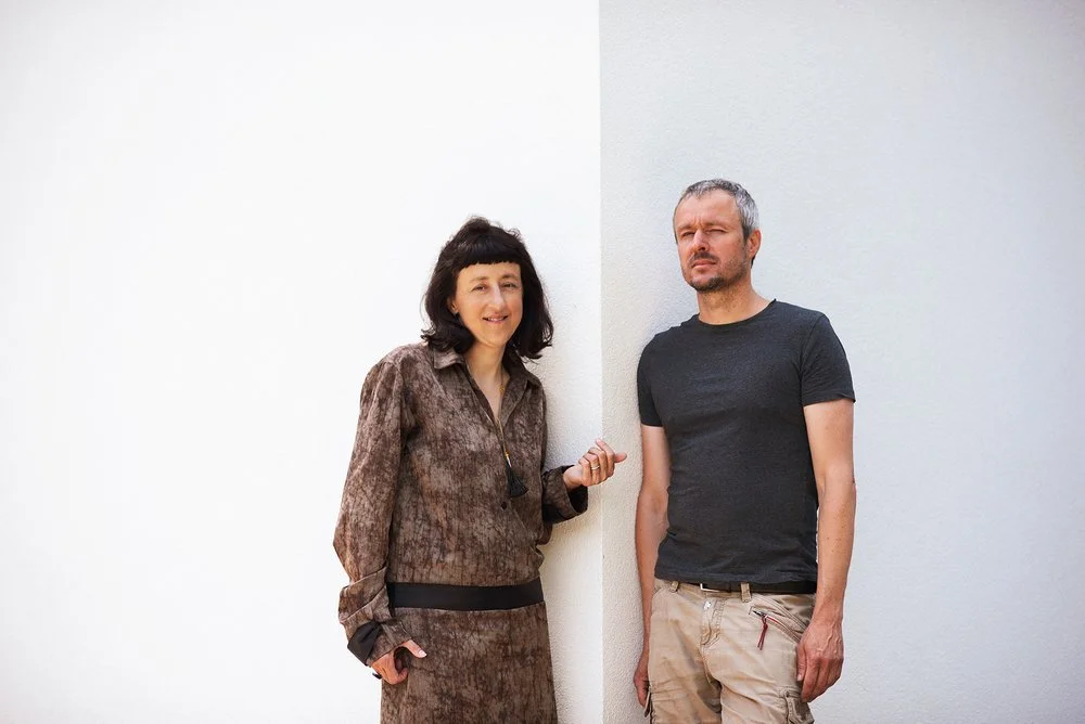 Dva lidé pózující před bílou stěnou, profesionální portrét pro prezentaci spolupráce nebo firemního týmu.