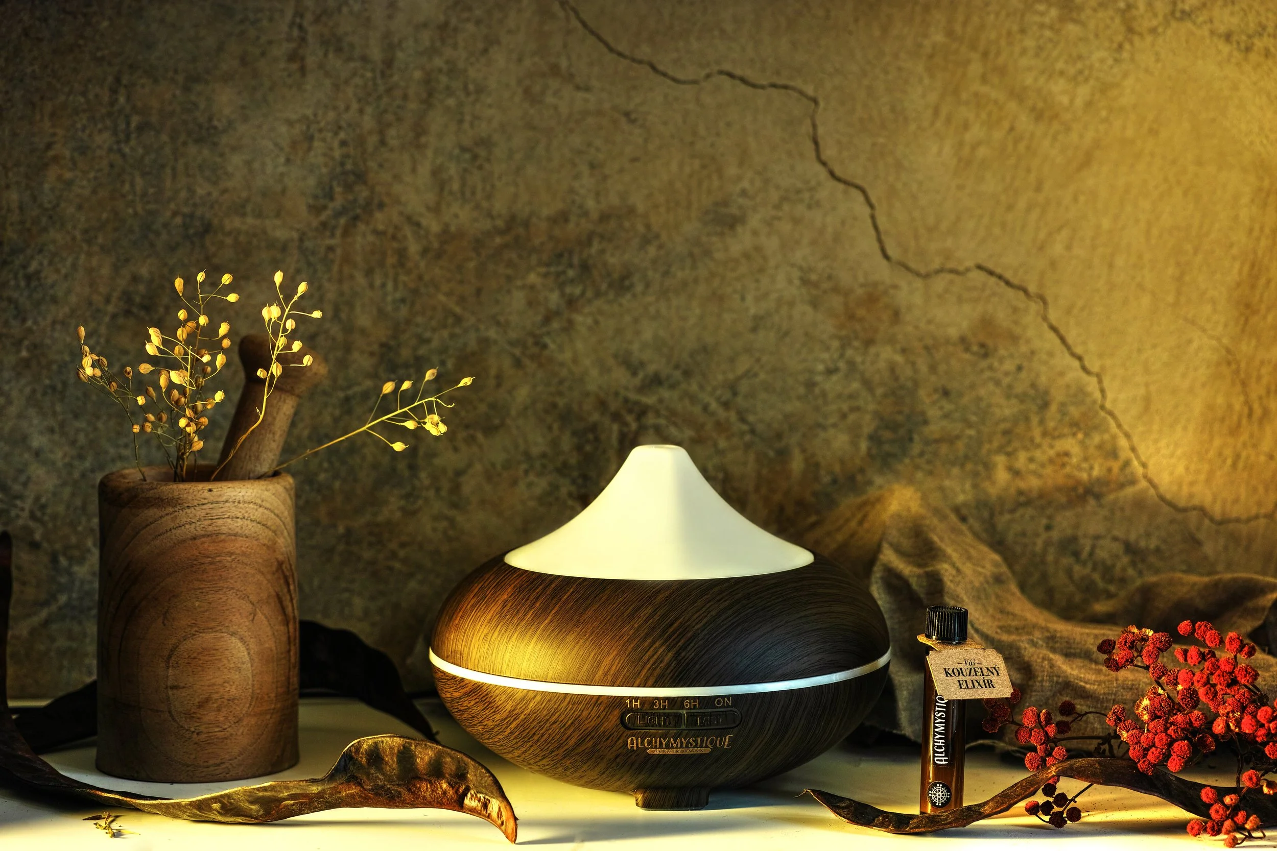 Dřevěný aromadifuzér s jemným osvětlením obklopený přírodní dekorací, esenciálním olejem a botanickými prvky, produktová lifestyle fotografie.