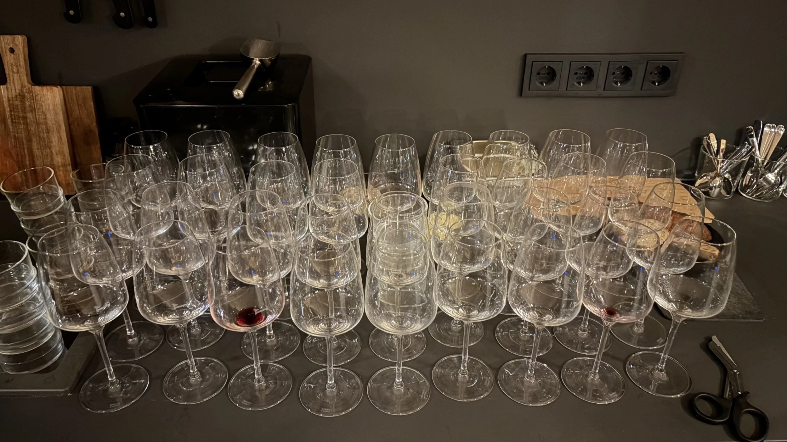Viele leere Weingläser auf einem Tisch, einige mit Resten von Rotwein auf einer schwarzen Oberfläche.