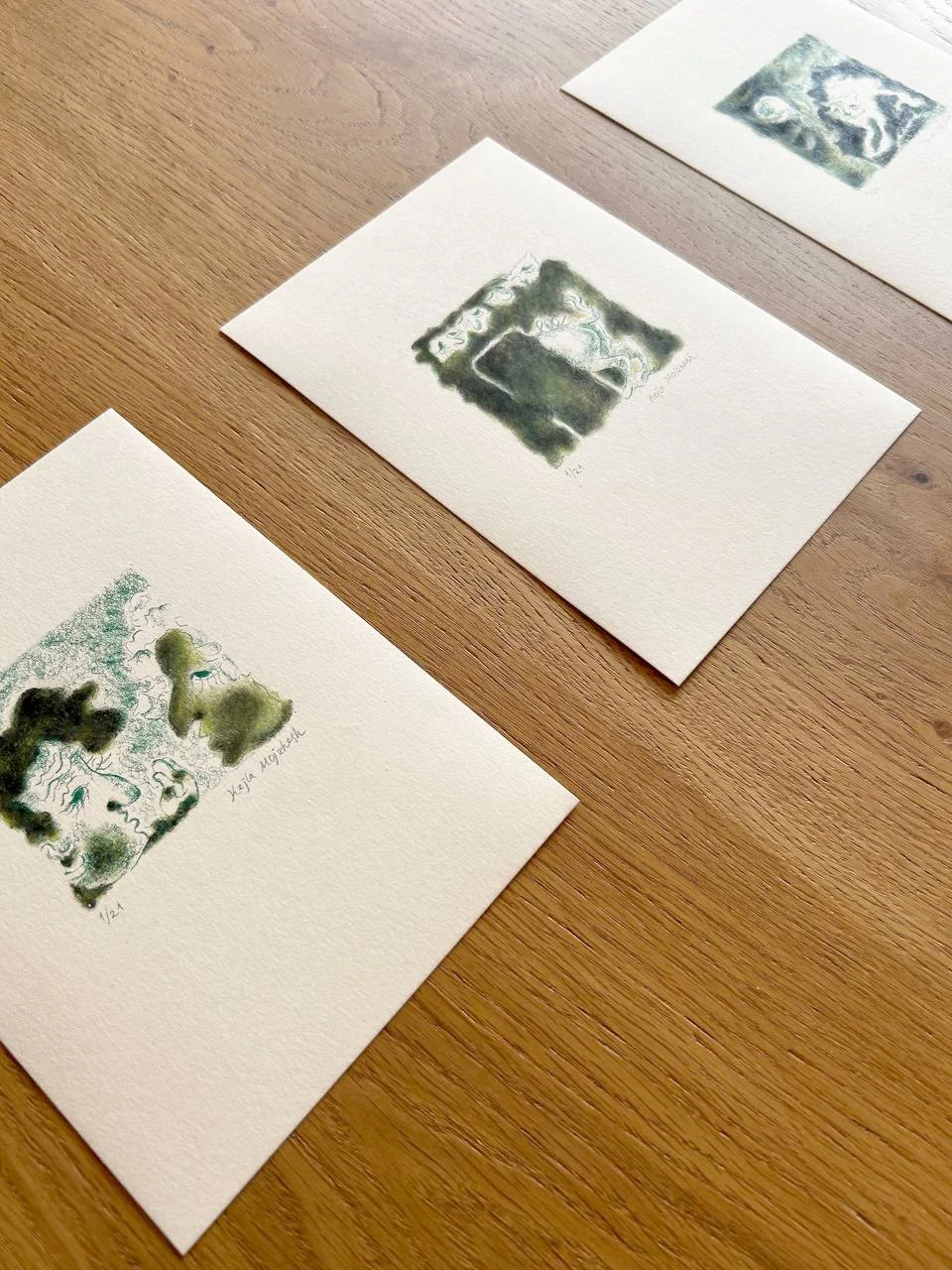 Three watercolor art prints with abstract and profile face designs on a wooden table.