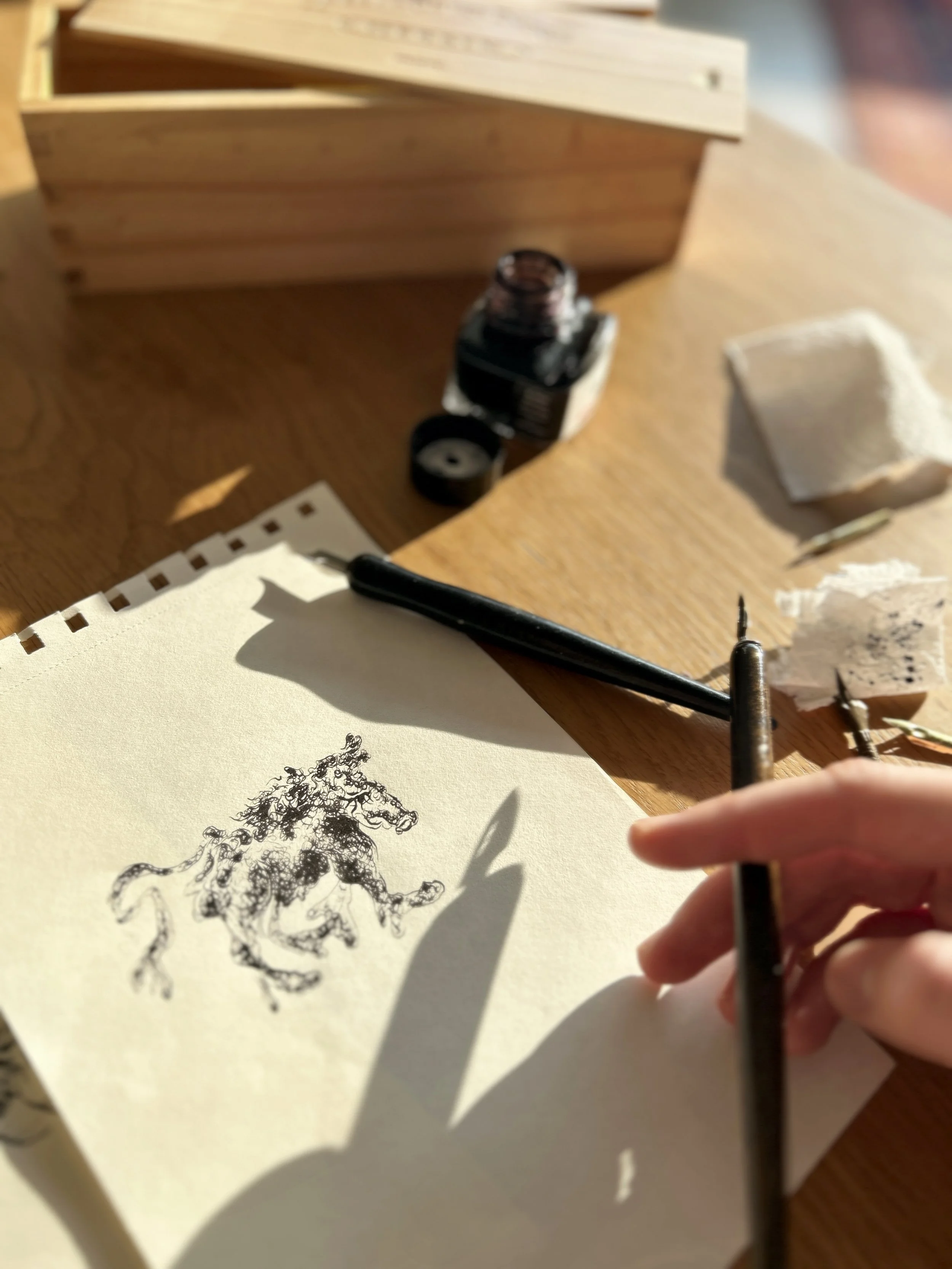 A hand holding a traditional calligraphy brush, drawing a detailed black ink sketch of a horse and rider on a piece of paper with a shadow cast from the brush.