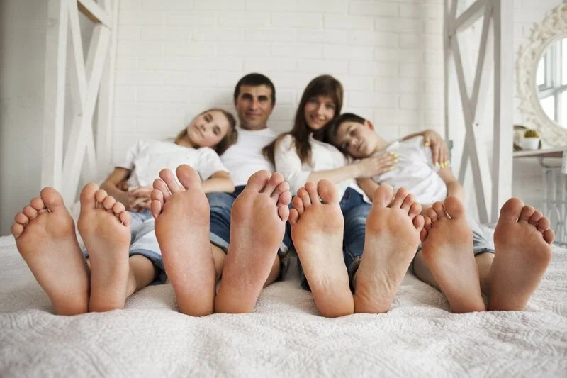 Happy family in bed with healthy feet exposed — family foot care, preventive podiatry, pediatric and adult foot health, custom orthotics and gait assessment at Canadian Foot Clinic & Orthotic Centre, St. Catharines.