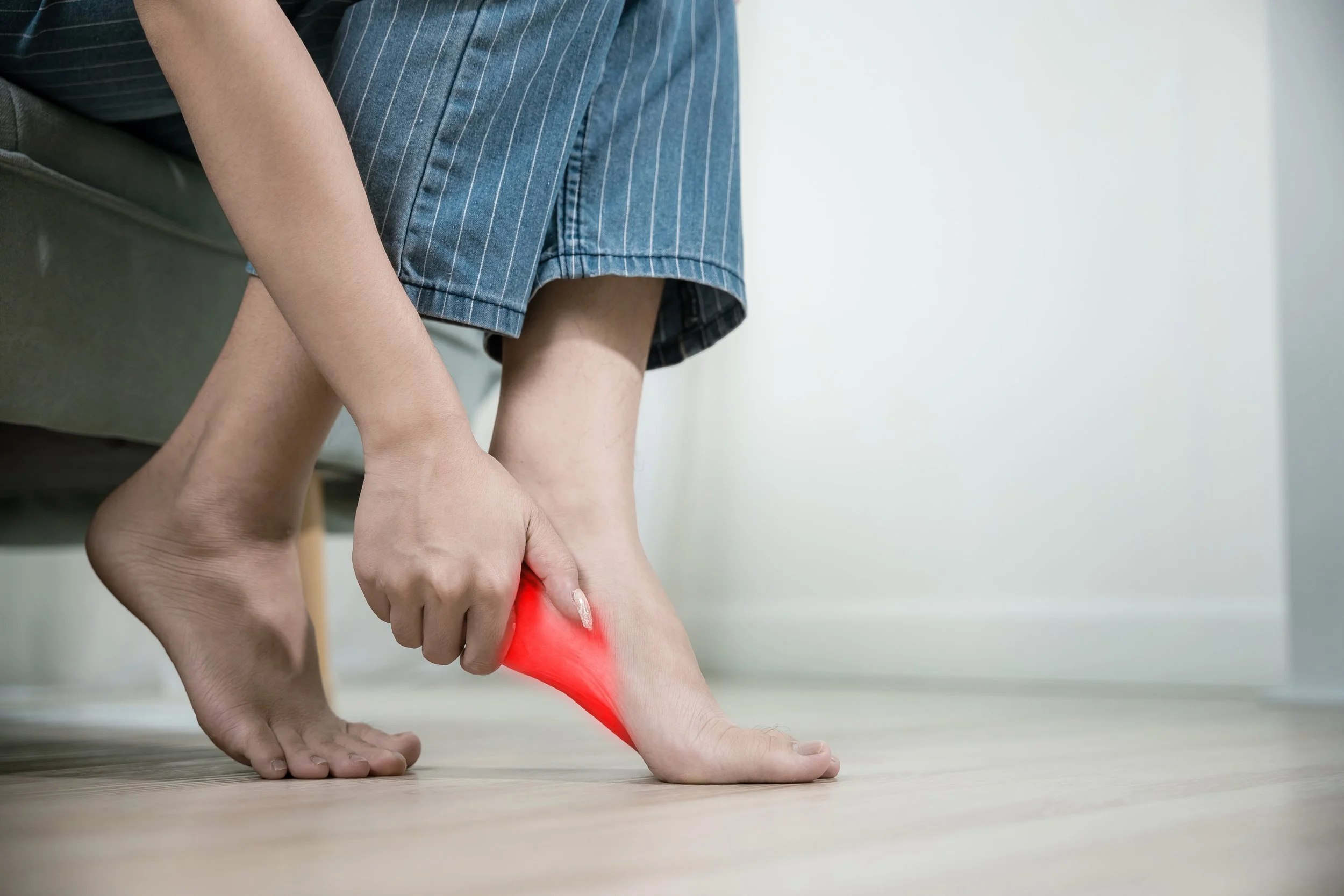 Woman clutching heel in pain — plantar fasciitis, heel pain, heel spurs; expert assessment, custom orthotics, shockwave therapy, heel relief by registered chiropodist at Canadian Foot Clinic & Orthotic Centre, St. Catharines.