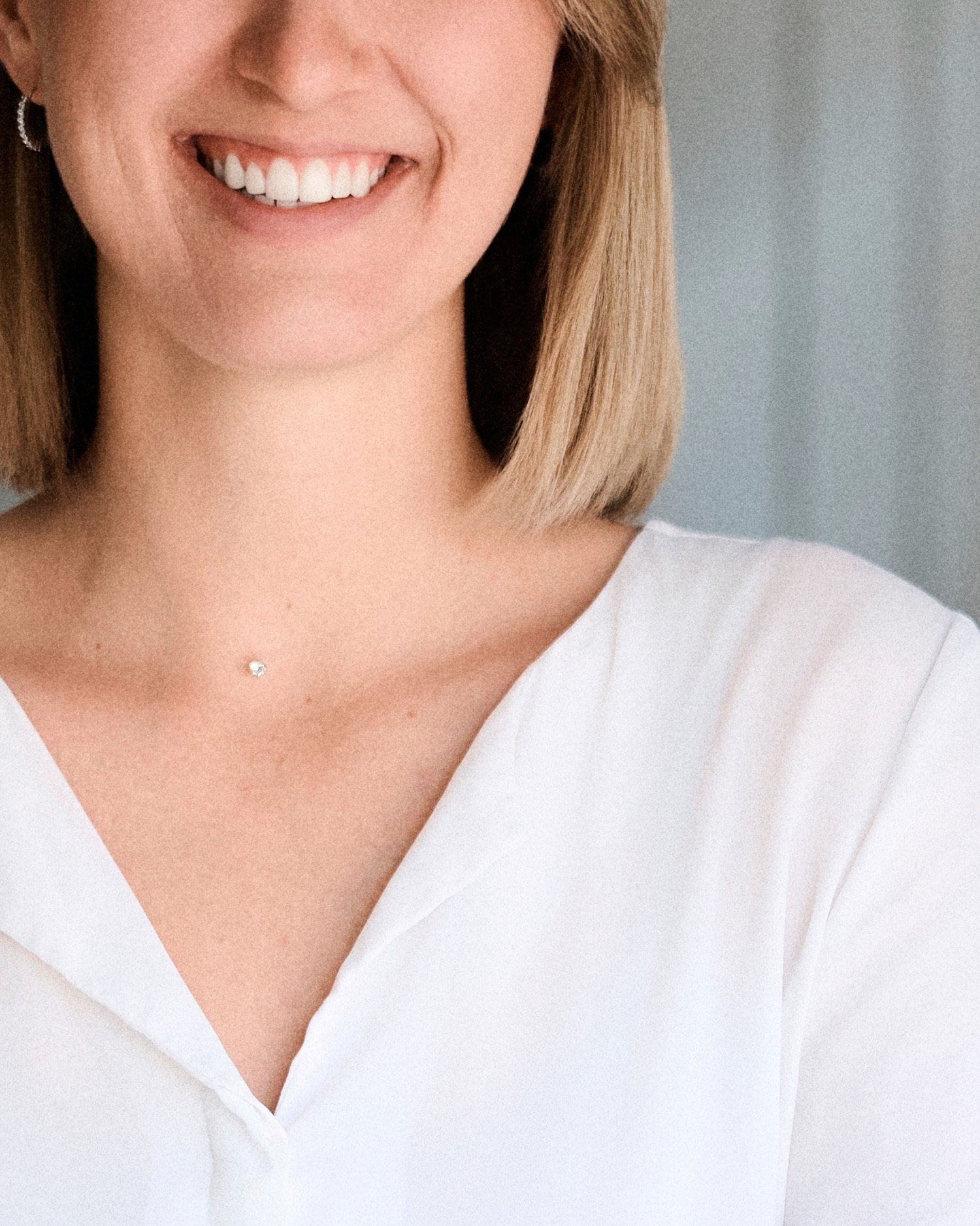 Nahaufnahme eines lachenden Frauenmunds, sichtbare Zähne, weiße Bluse, kurze braune Haare, silberne Ohrringe, silberne Kette