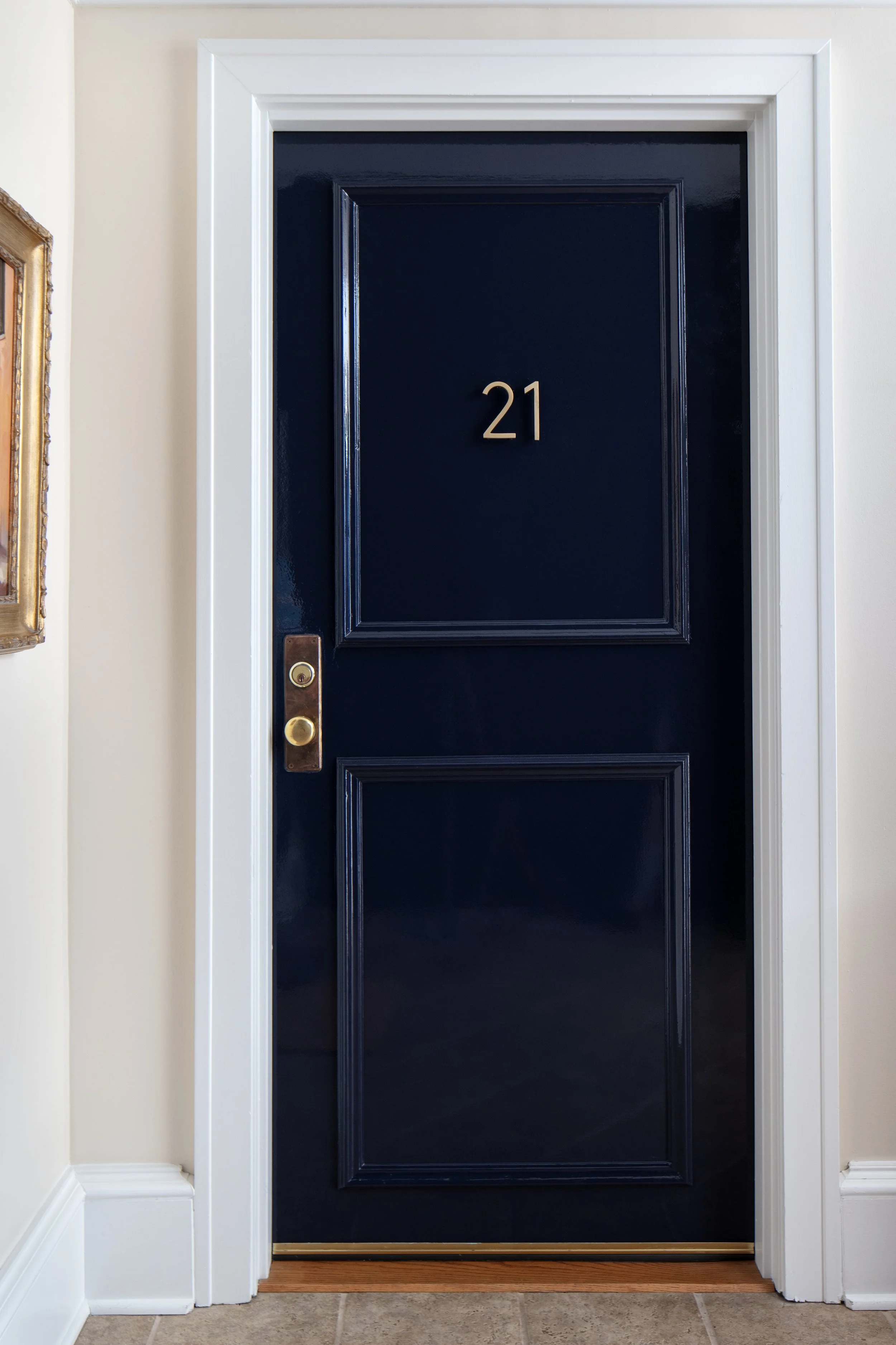 Interior view of a dark blue front door with the number 21, brass door handle, and white trim.