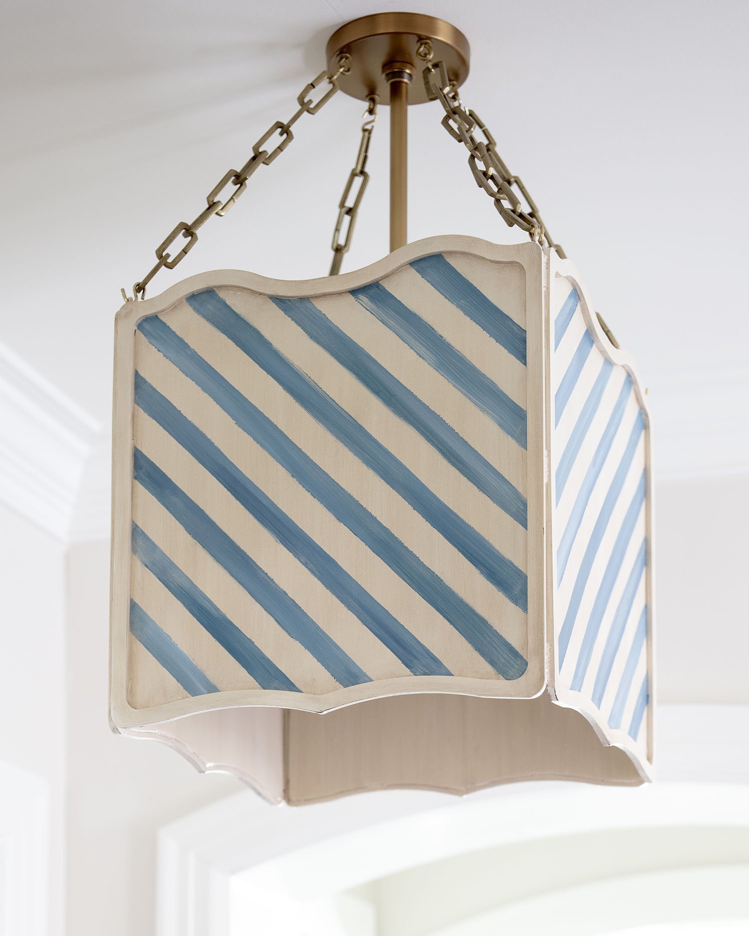 A decorative wooden lampshade with blue and beige stripes, hanging from a ceiling by a chain.