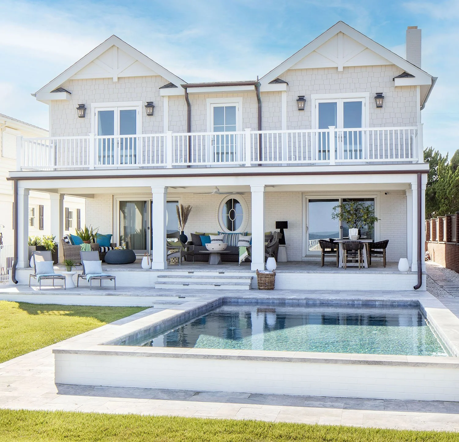 Two-story modern house with white exterior, large balcony, outdoor seating, and a swimming pool in the backyard
