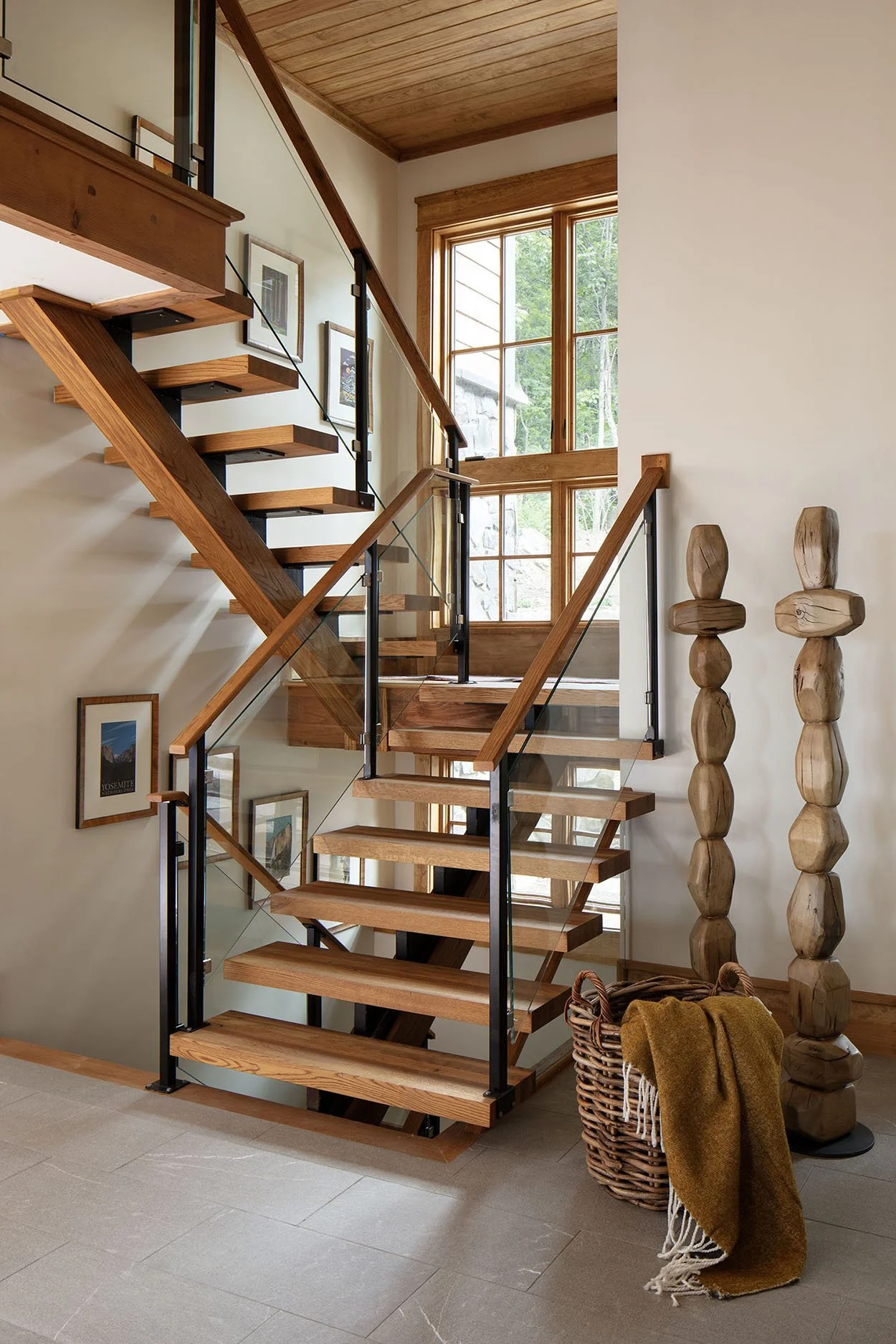 Interior view of a modern wooden staircase with glass railing, natural wood finish, and large windows letting in natural light.