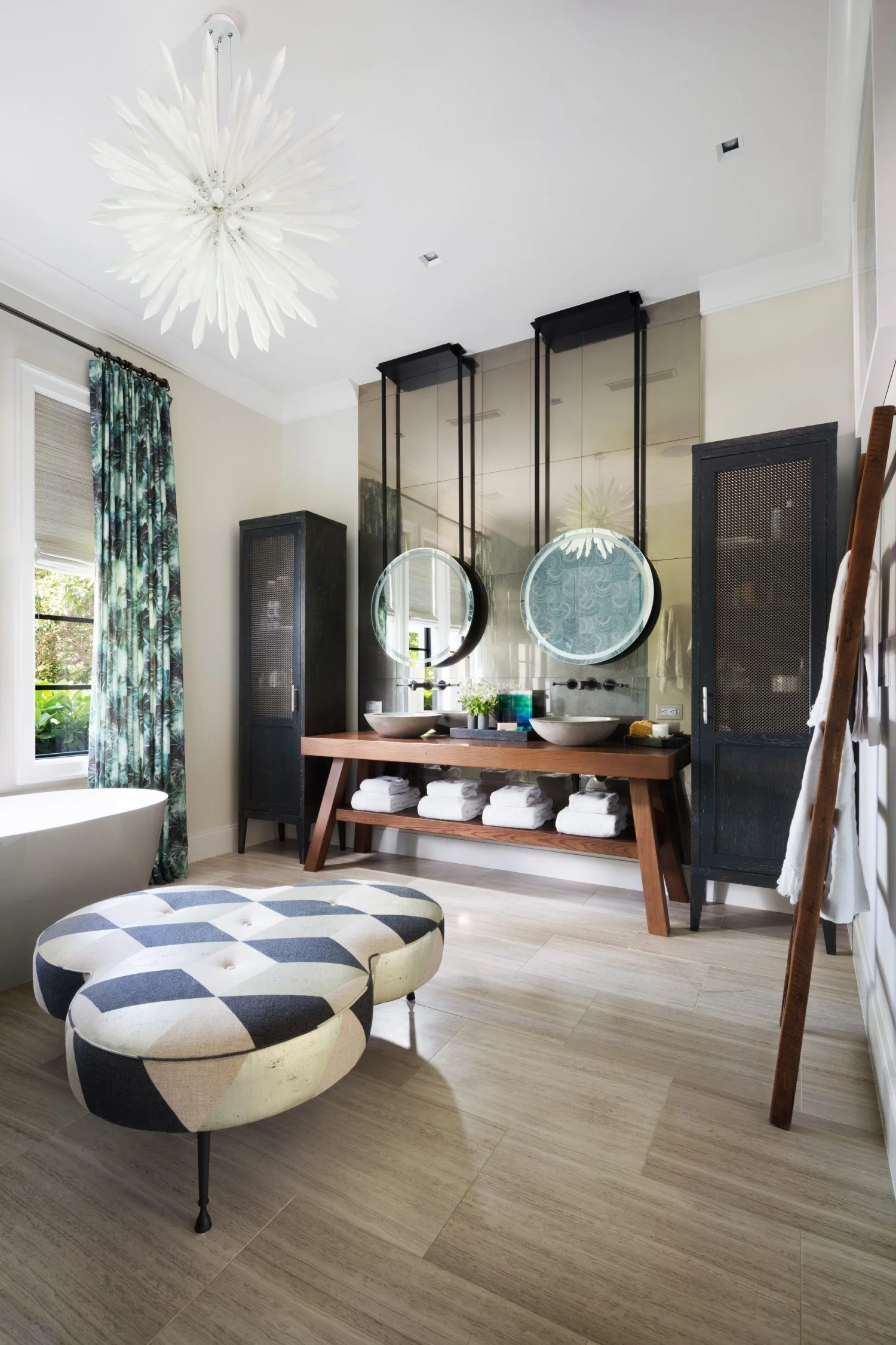Modern bathroom with dual sinks, round mirrors, black cabinets, and a bathtub near a window with patterned curtains.
