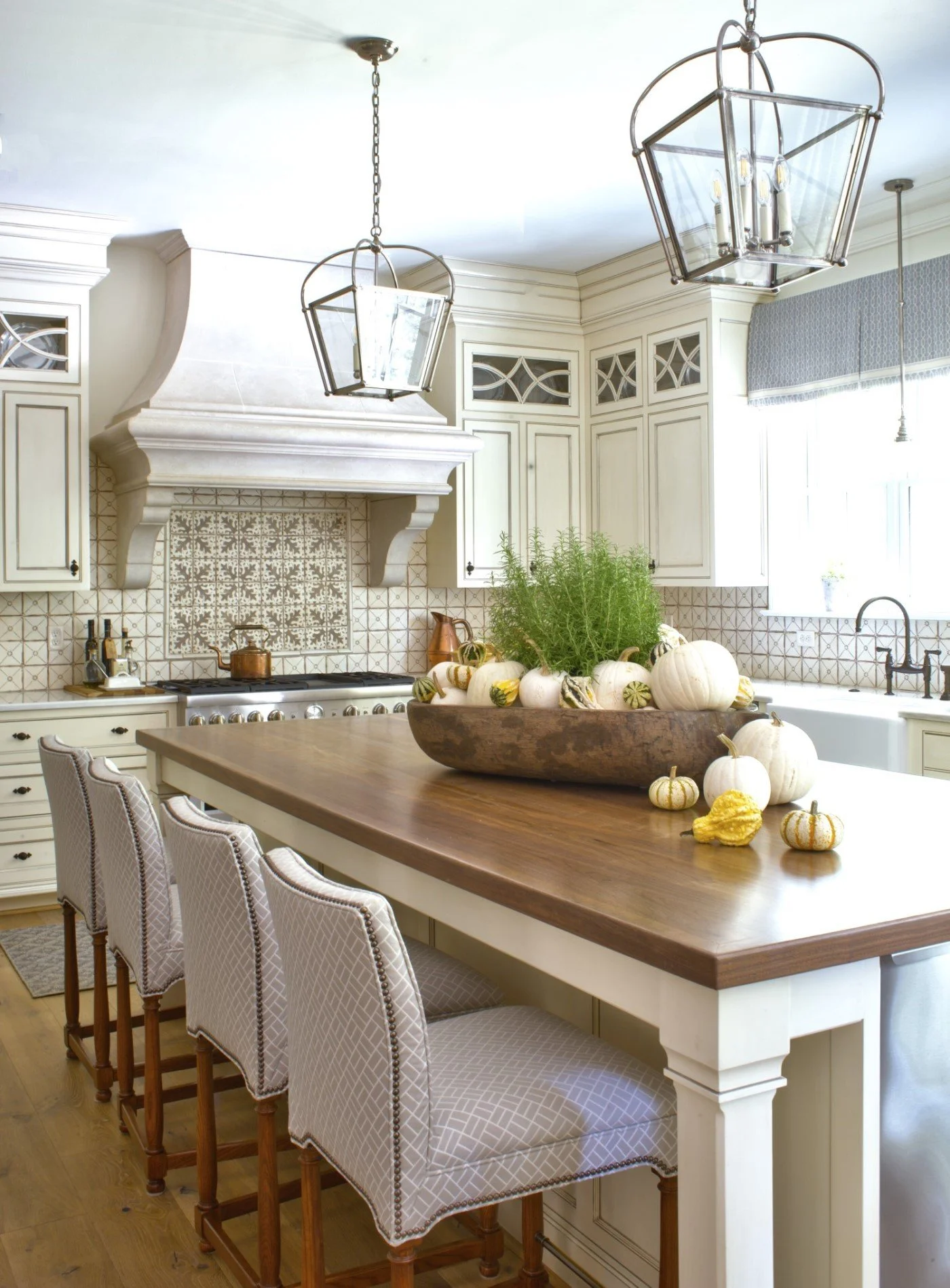 A bright kitchen with white cabinetry, a large wooden island with pumpkins and greenery, and two pendant lights hanging from the ceiling.