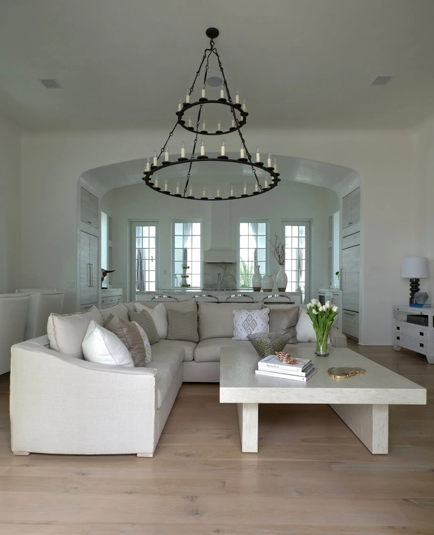Living room with a large white sectional sofa, a rectangular coffee table with flowers, and a black chandelier with candles hanging from the ceiling.