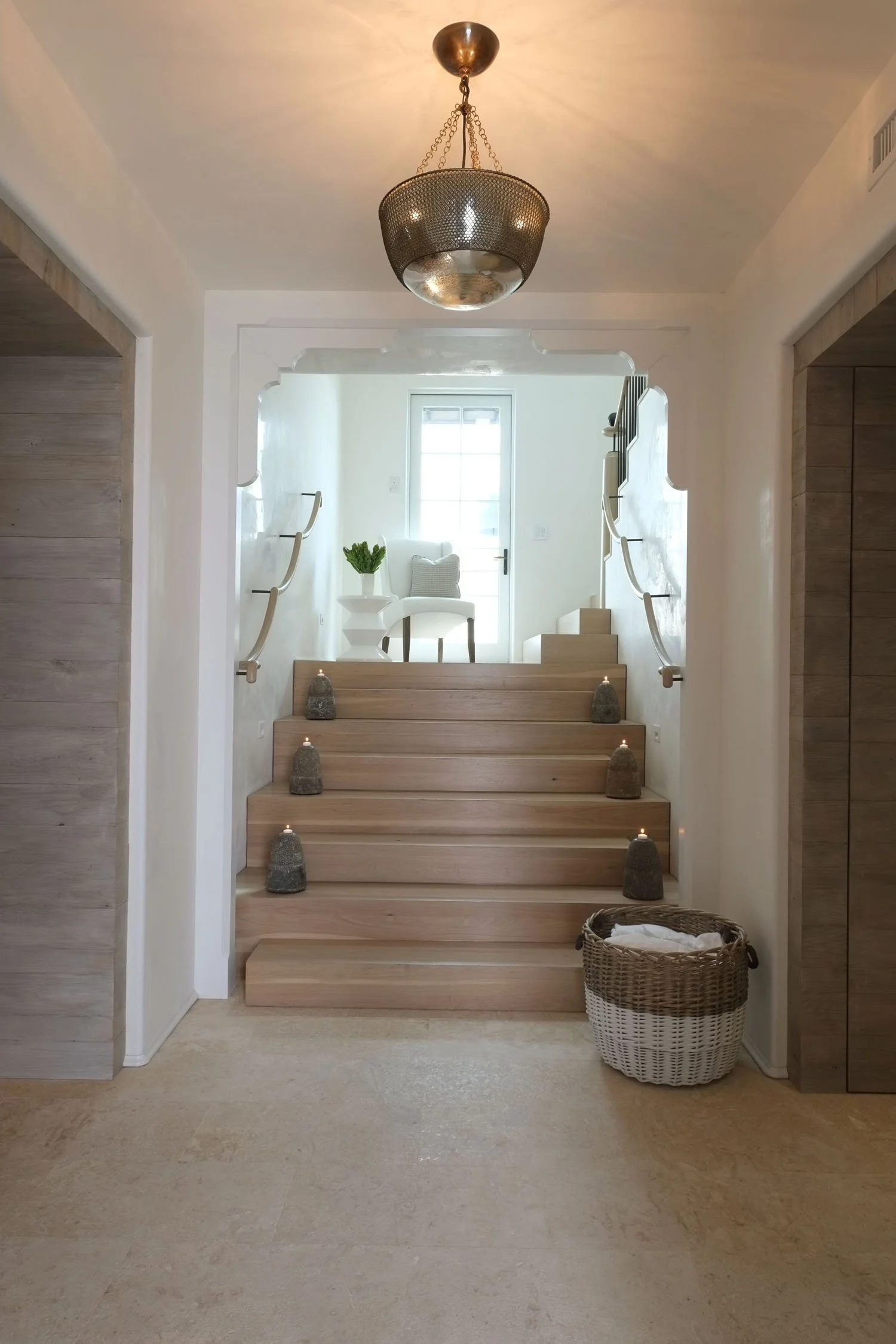 Wooden stairs with small candles on each step leading up to a white sitting area with a chair, pillow, and potted plant, and a window in the background.