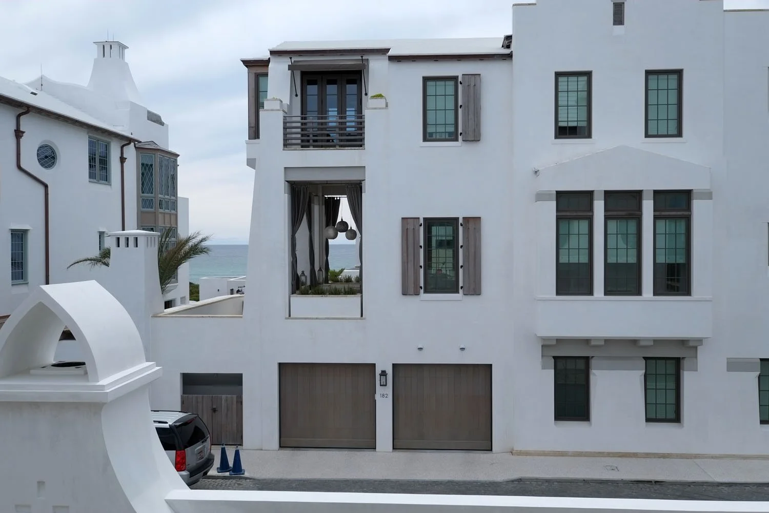White modern residential building with multiple windows, balconies, and a garage, near the ocean under a cloudy sky.