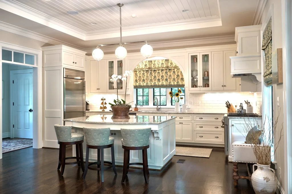 Bright, white kitchen with island, pendant lights, sunflower decorations, and a window with patterned valance.