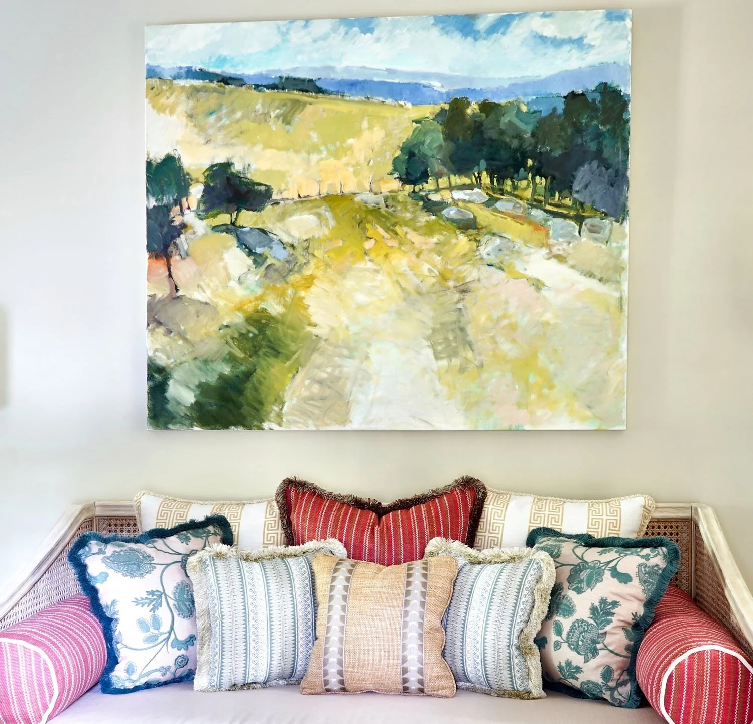 A living room with a large landscape painting hung above a sofa decorated with various patterned cushions.