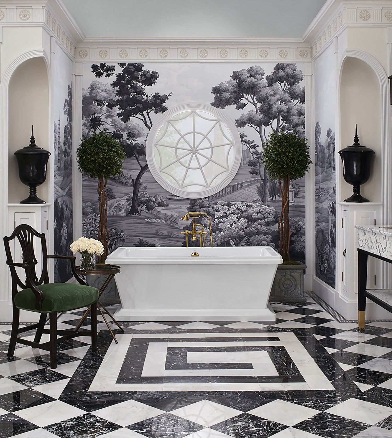 Elegant bathroom with a white bathtub, black and white landscape mural, checkered marble floor, greenery, gold fixtures, and black urns.