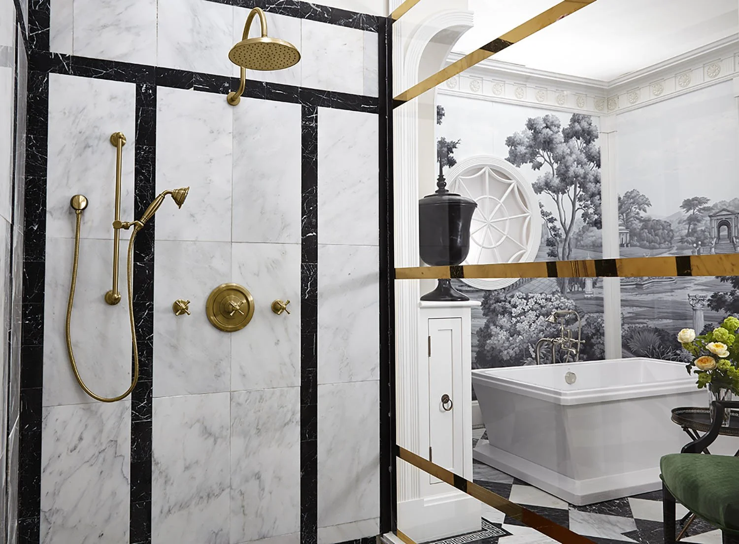 A luxurious bathroom with a marble shower area featuring gold fixtures and a separate bathtub in a room with ornate wallpaper depicting a scenic landscape.