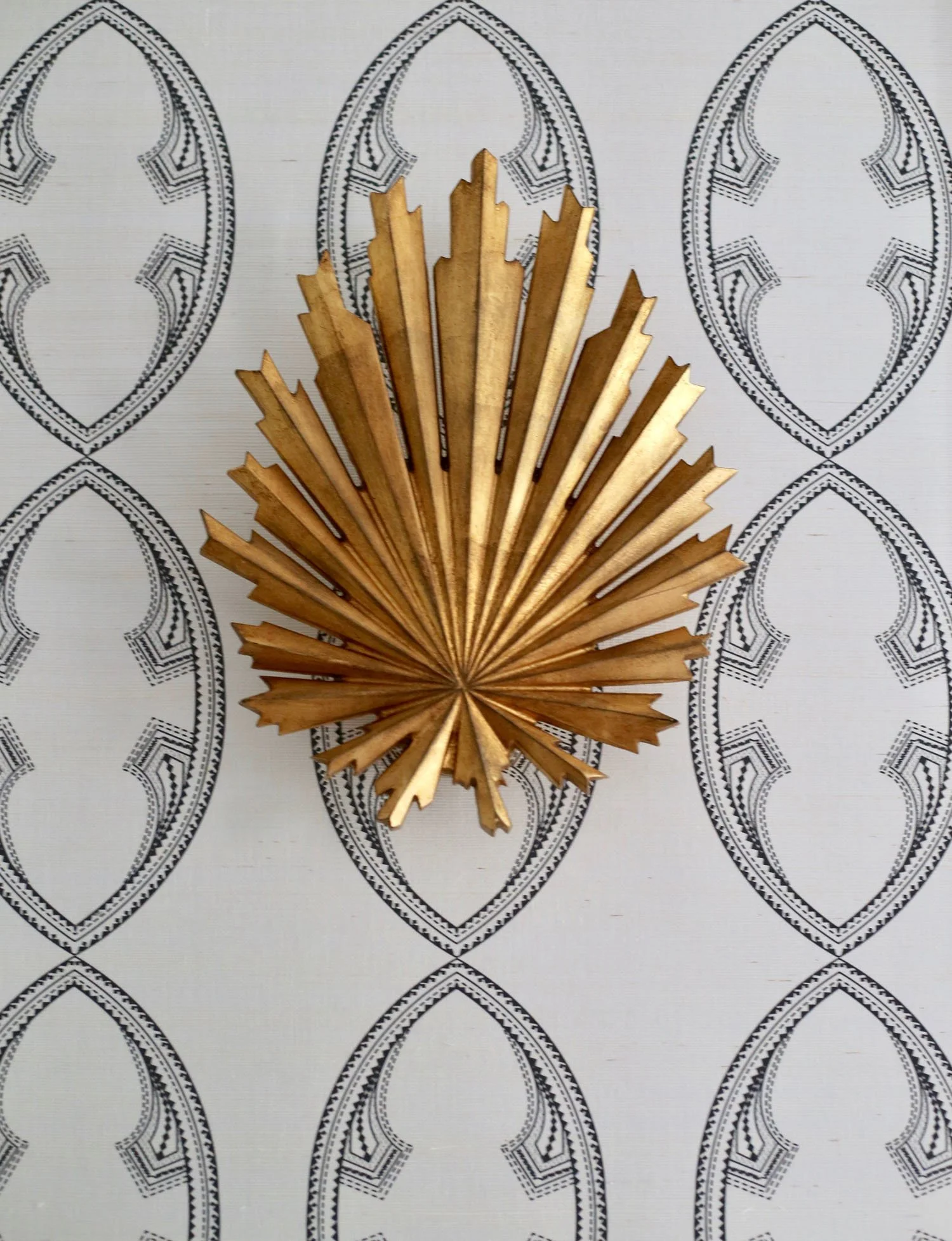 Decorative wooden leaf-shaped fan on patterned white and black background.