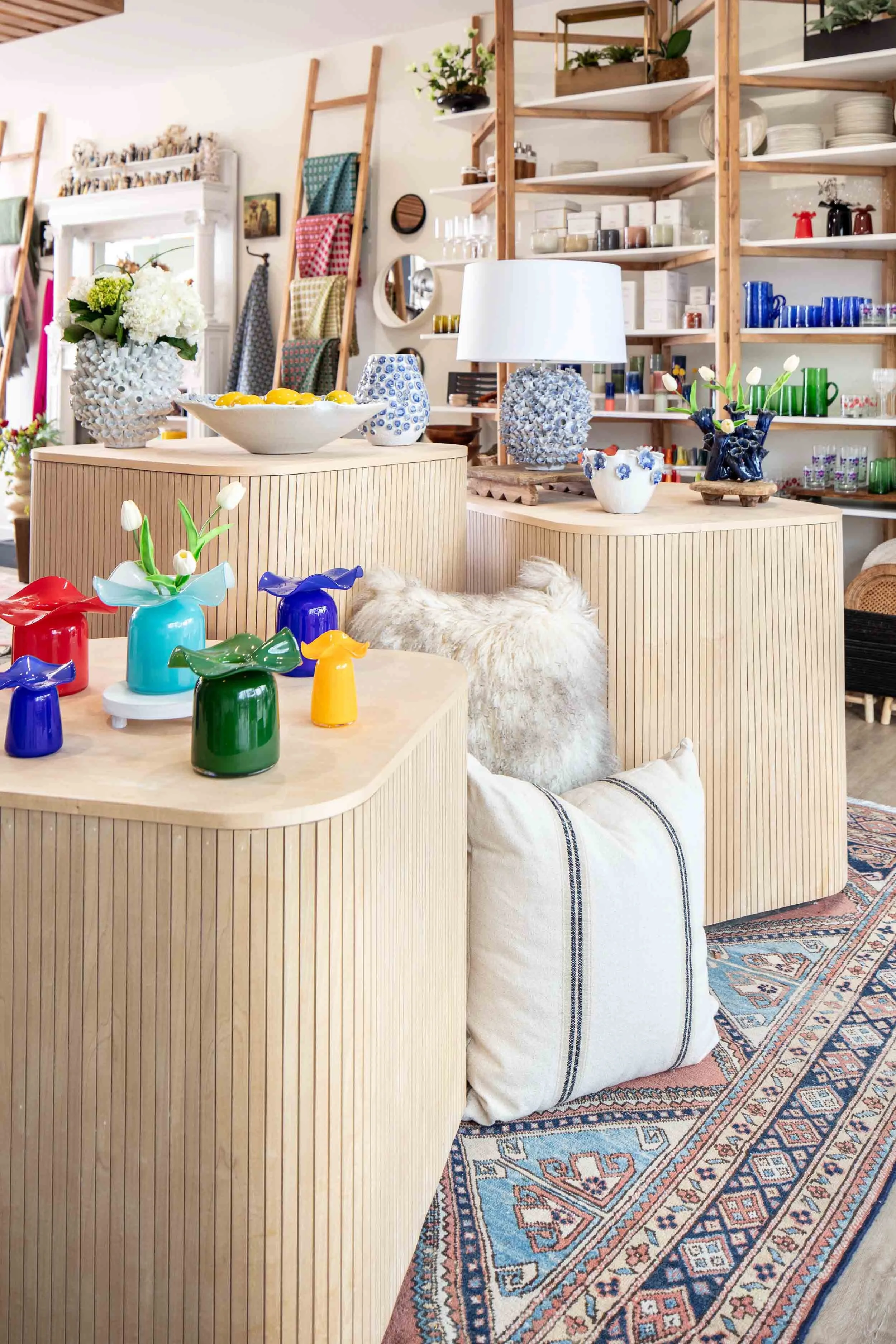 Interior of a store or living space with wooden furniture, decorative vases, and colorful ceramics, with walls adorned with shelves of various items, and a patterned rug on the floor.