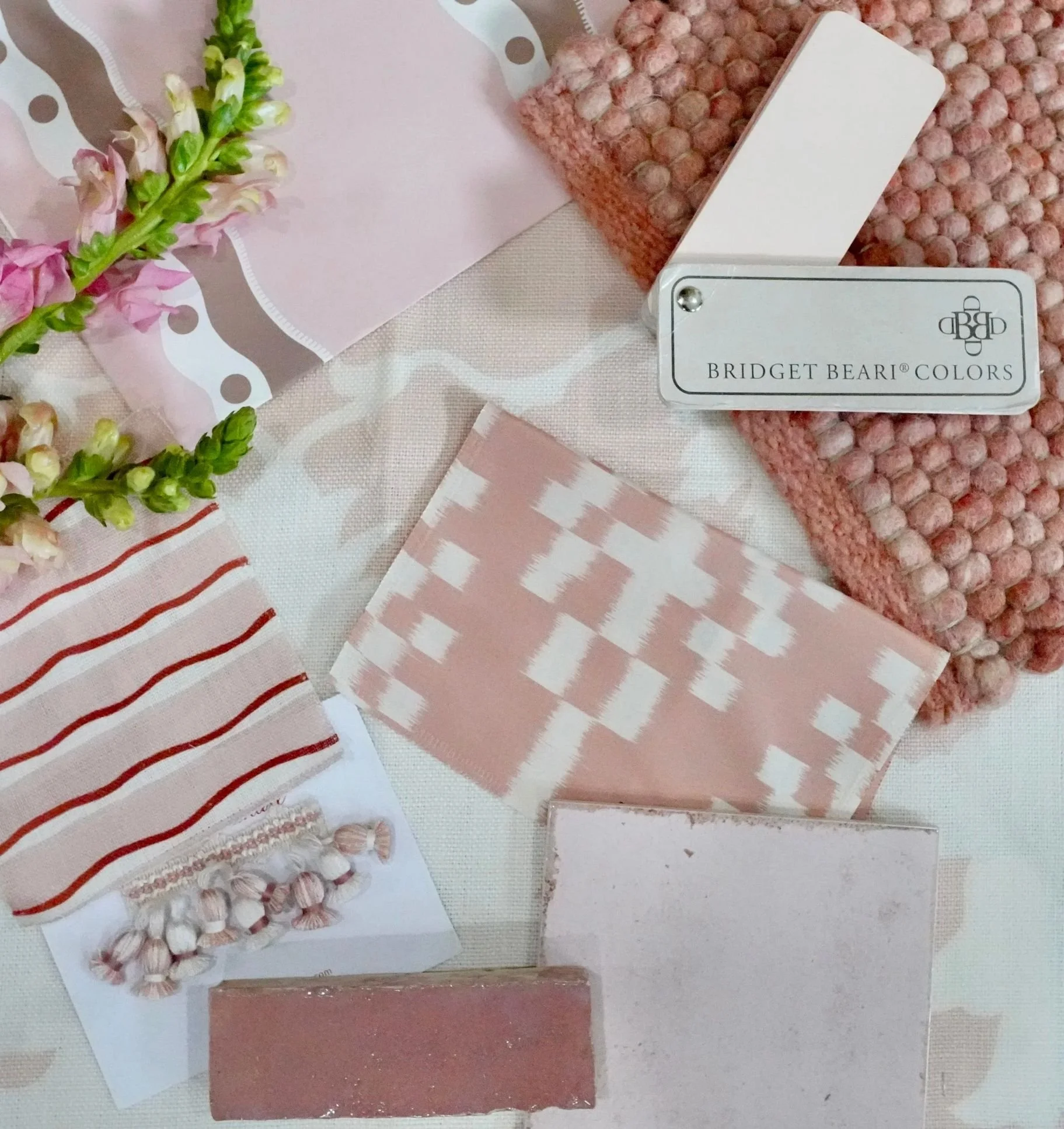 An array of pink fabrics and paint cards lay flat, with 2 pink tiles and a pink fringe at the bottom.