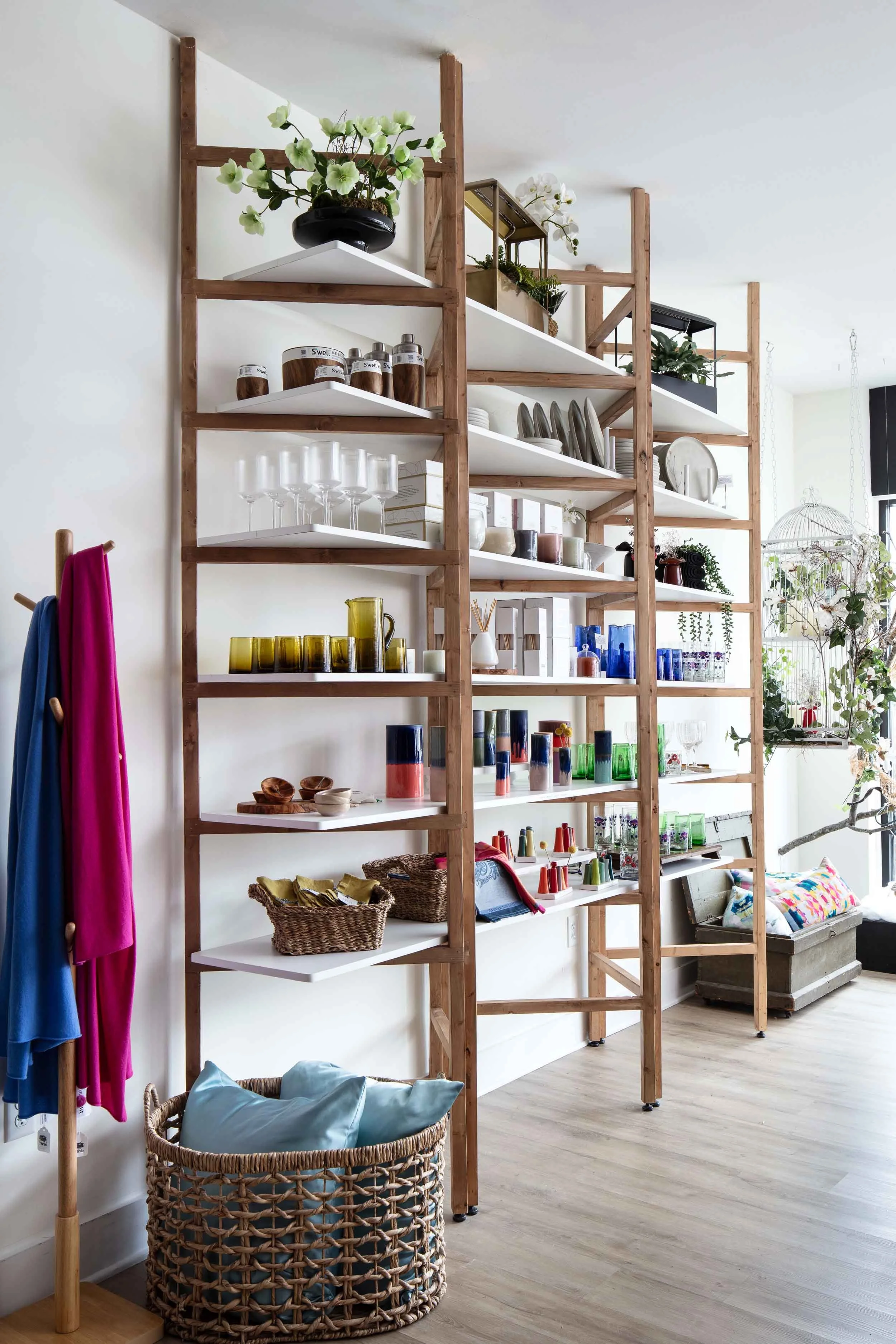 Open wooden and white shelving unit displaying various decorative items, glassware, and plants in a bright living space.