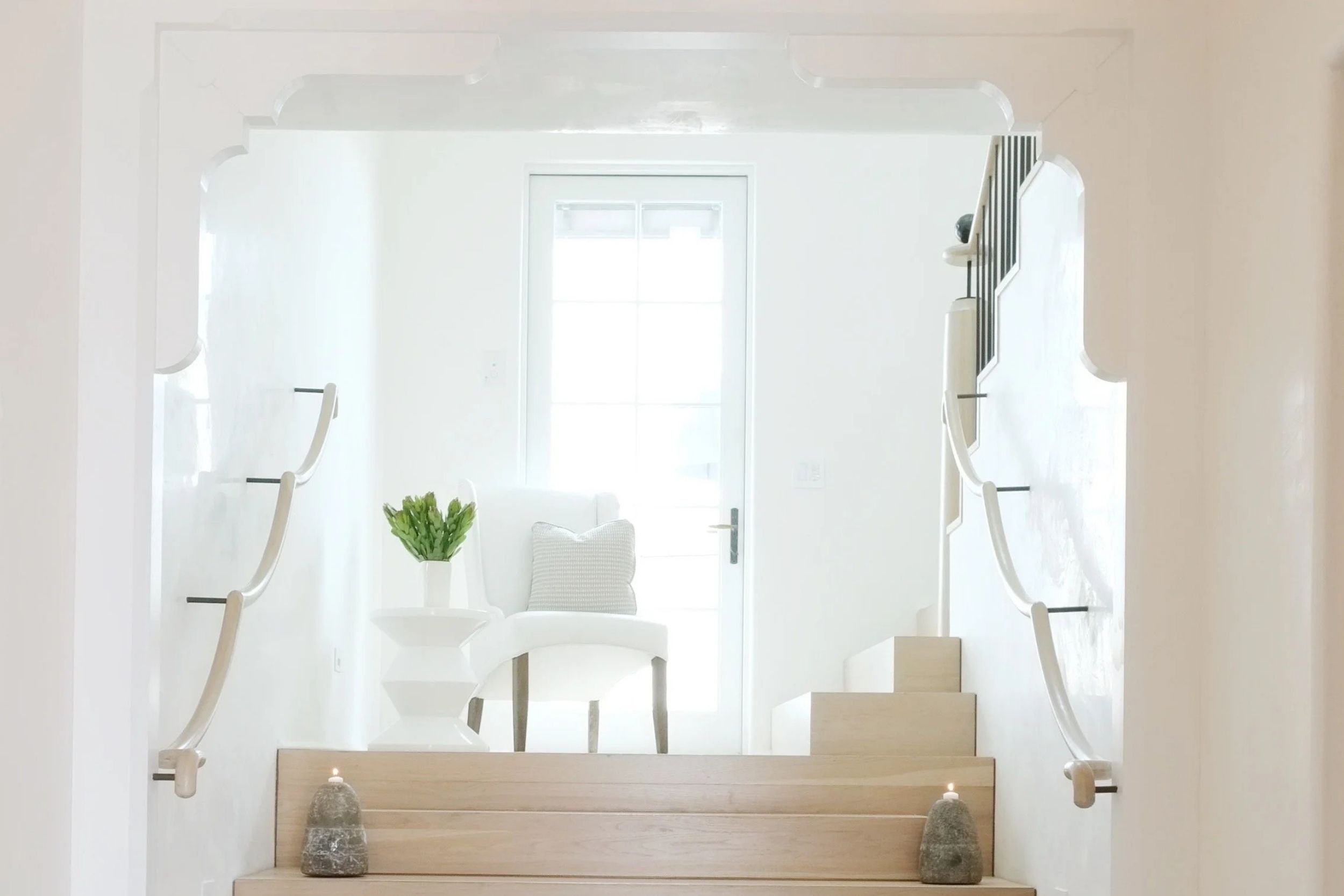 White walls, handrails, a chair and a side table look bright and airy in this foyer, with the light wood stairs adding depth.