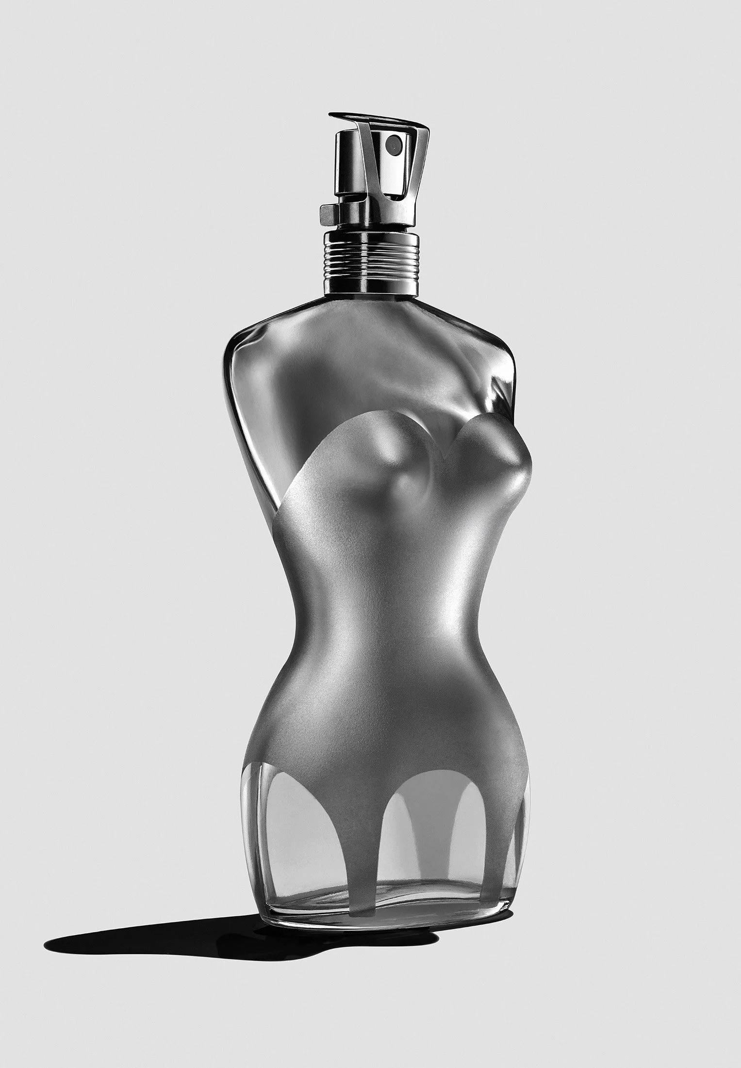 A clear glass spray bottle with a metallic cap and nozzle, positioned against a plain light background, casting a shadow.