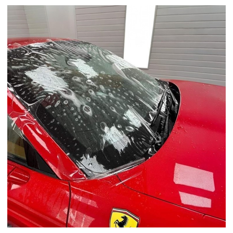 A red Ferrari car with foam soap and water on the windshield, likely in the process of being washed.