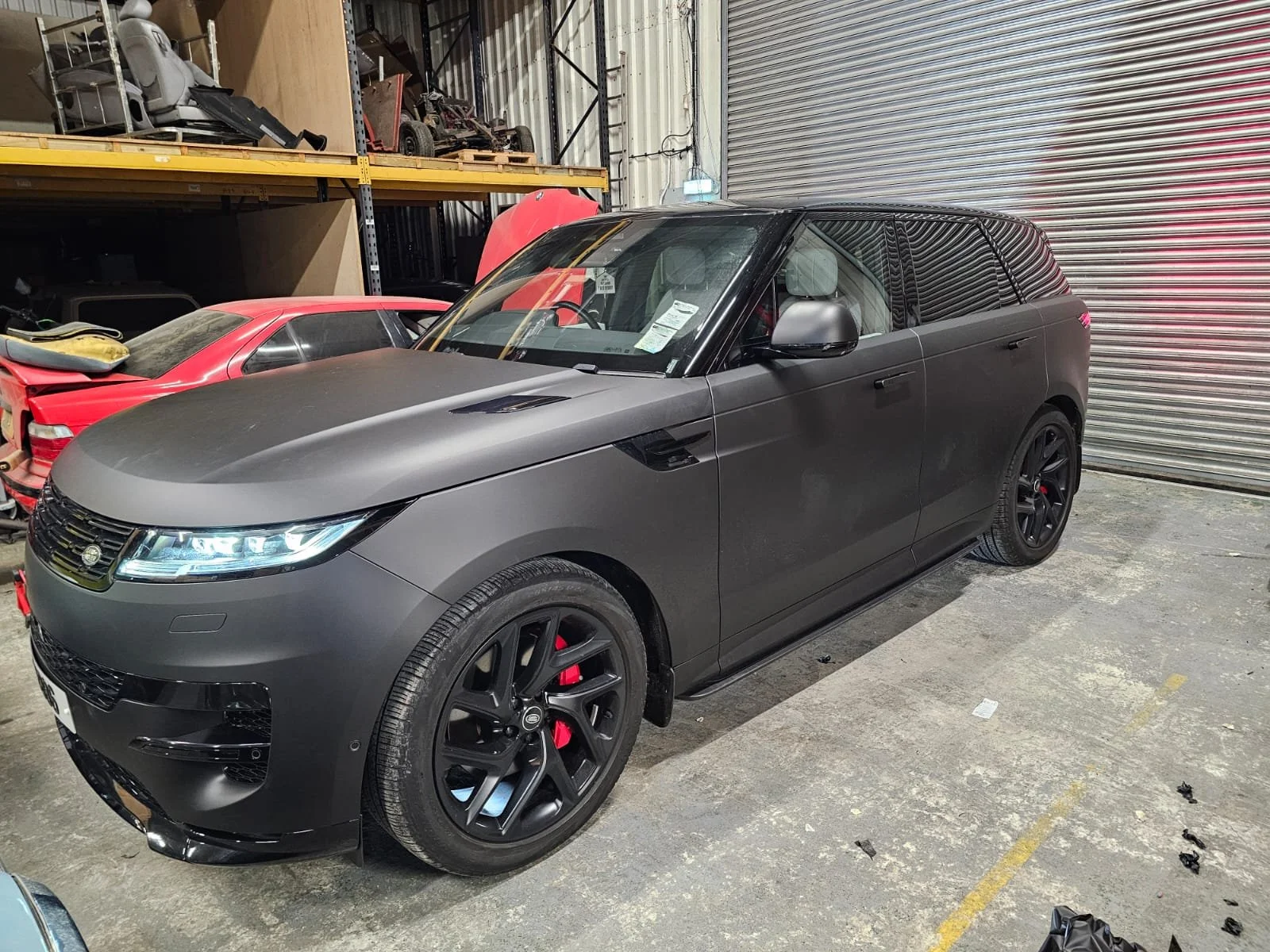 A matte black Range Rover SUV parked inside a warehouse, surrounded by other vehicles and storage shelves.