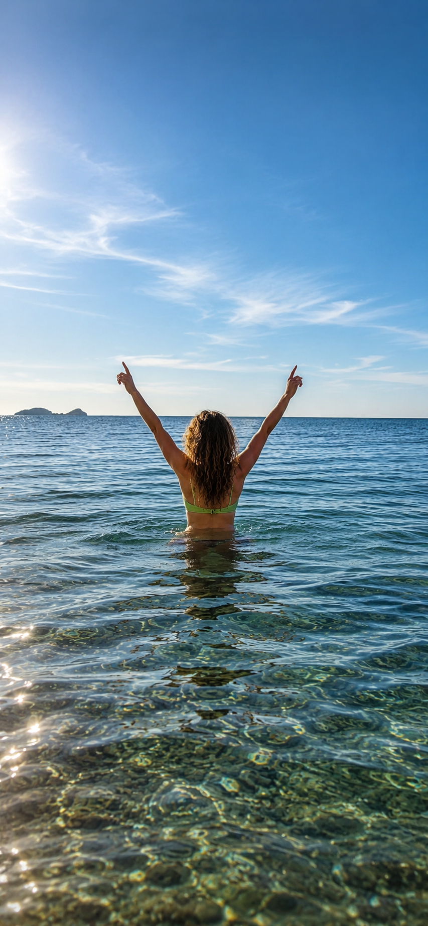 Woman in a yellow swimsuit raising her arms in the ocean with clear water and blue sky.