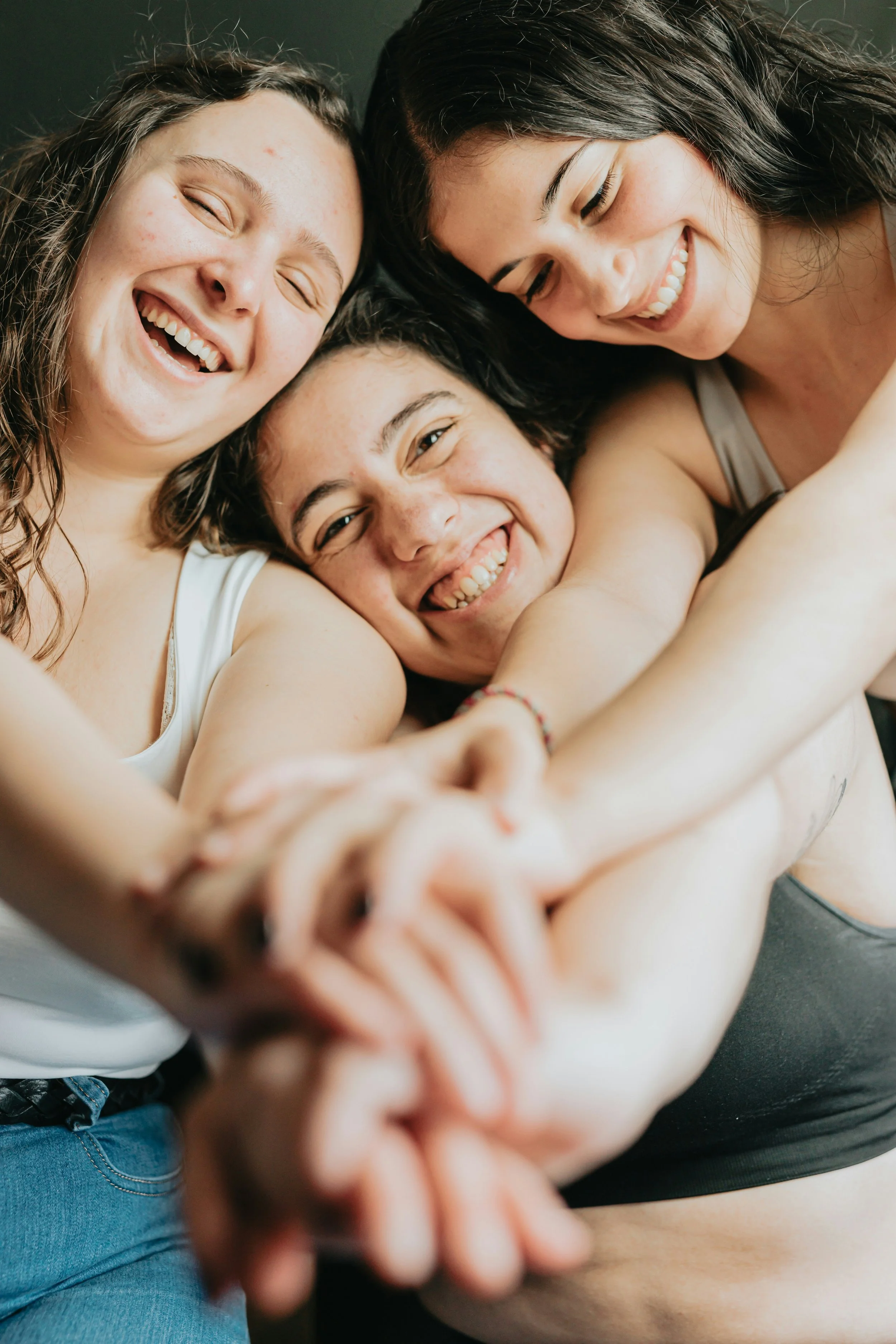 Three young women smiling and embracing each other, taking a selfie together.