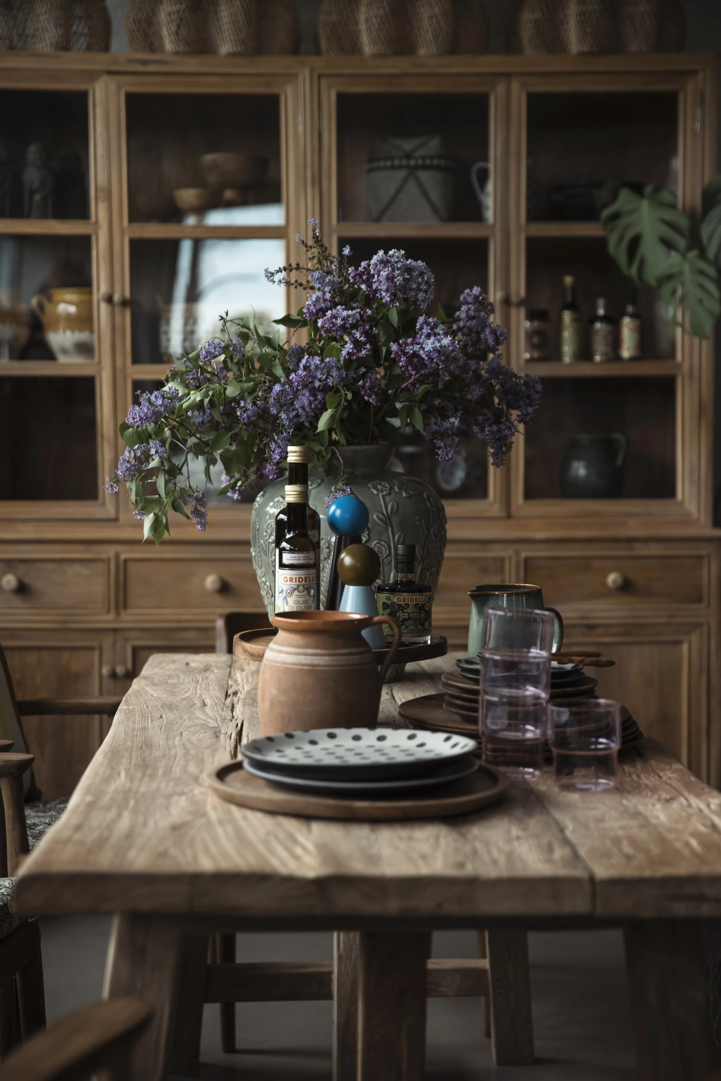 Ett träbord dekorerat med blommor, tallrikar, glas och flaskor, med ett skåp i trä i bakgrunden.