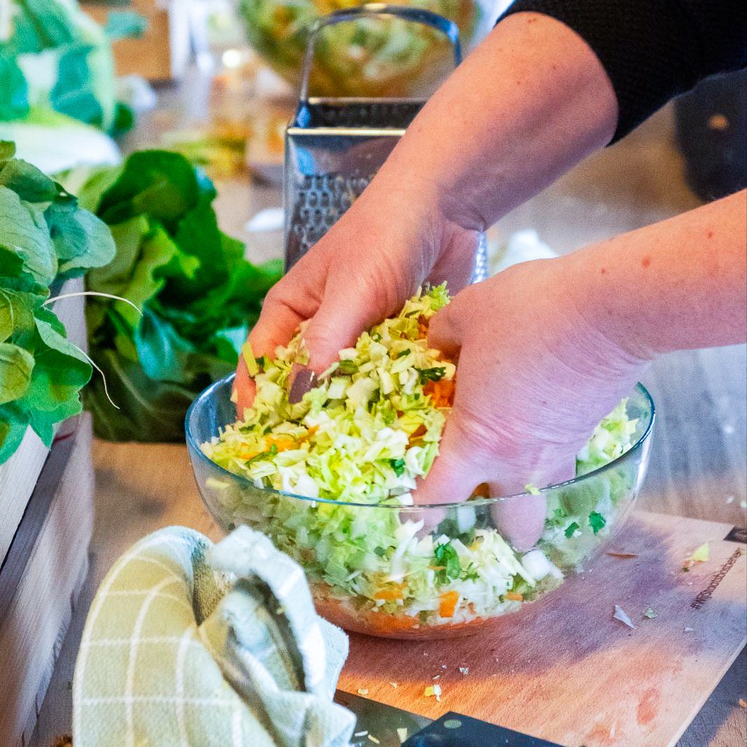 Personen die een kom met gesneden groenten, zoals kool en wortels, mengt in een keuken.