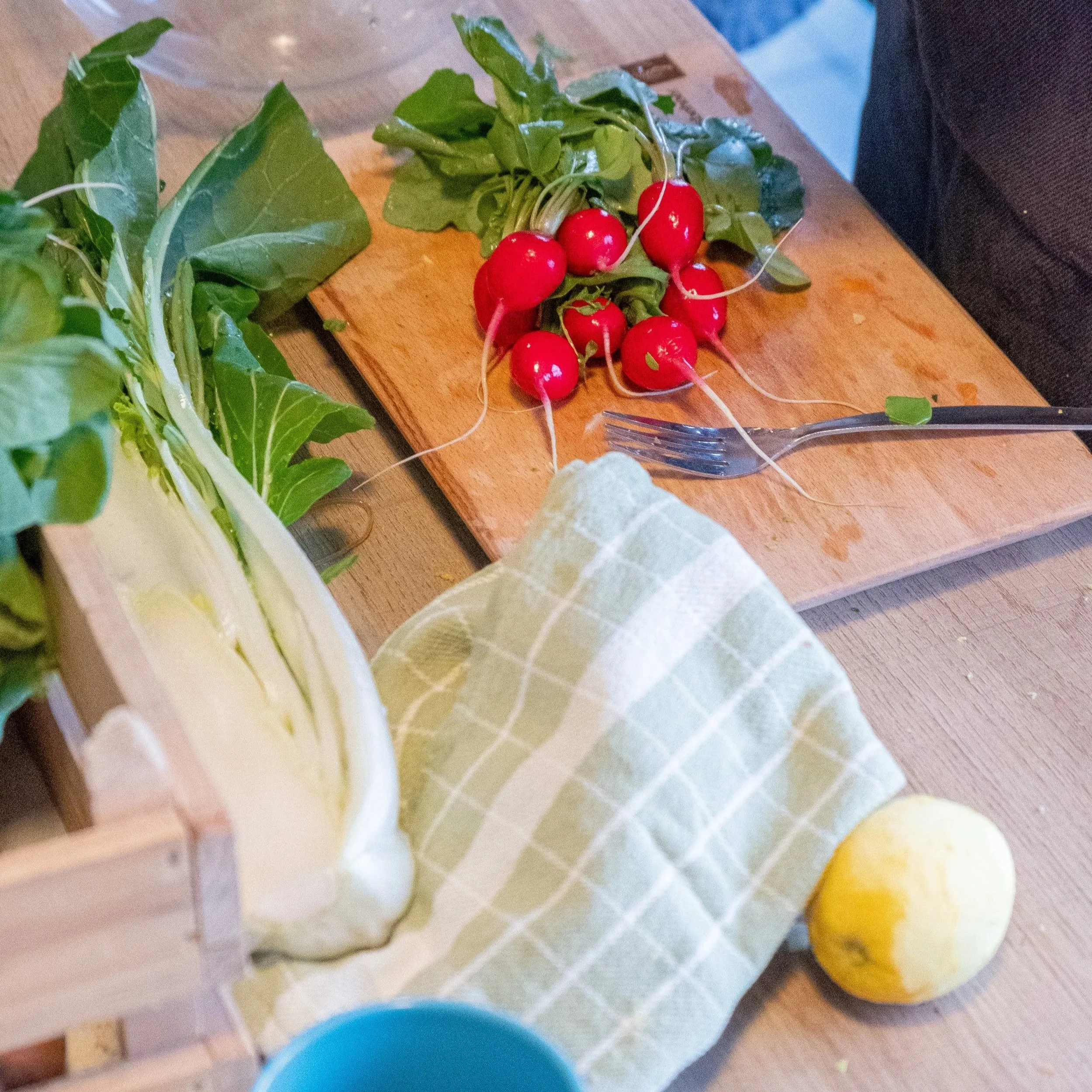 Radijsjes, groene bladgroenten en een citroen op een houten tafel met keukenaccessoires, klaar om te koken.