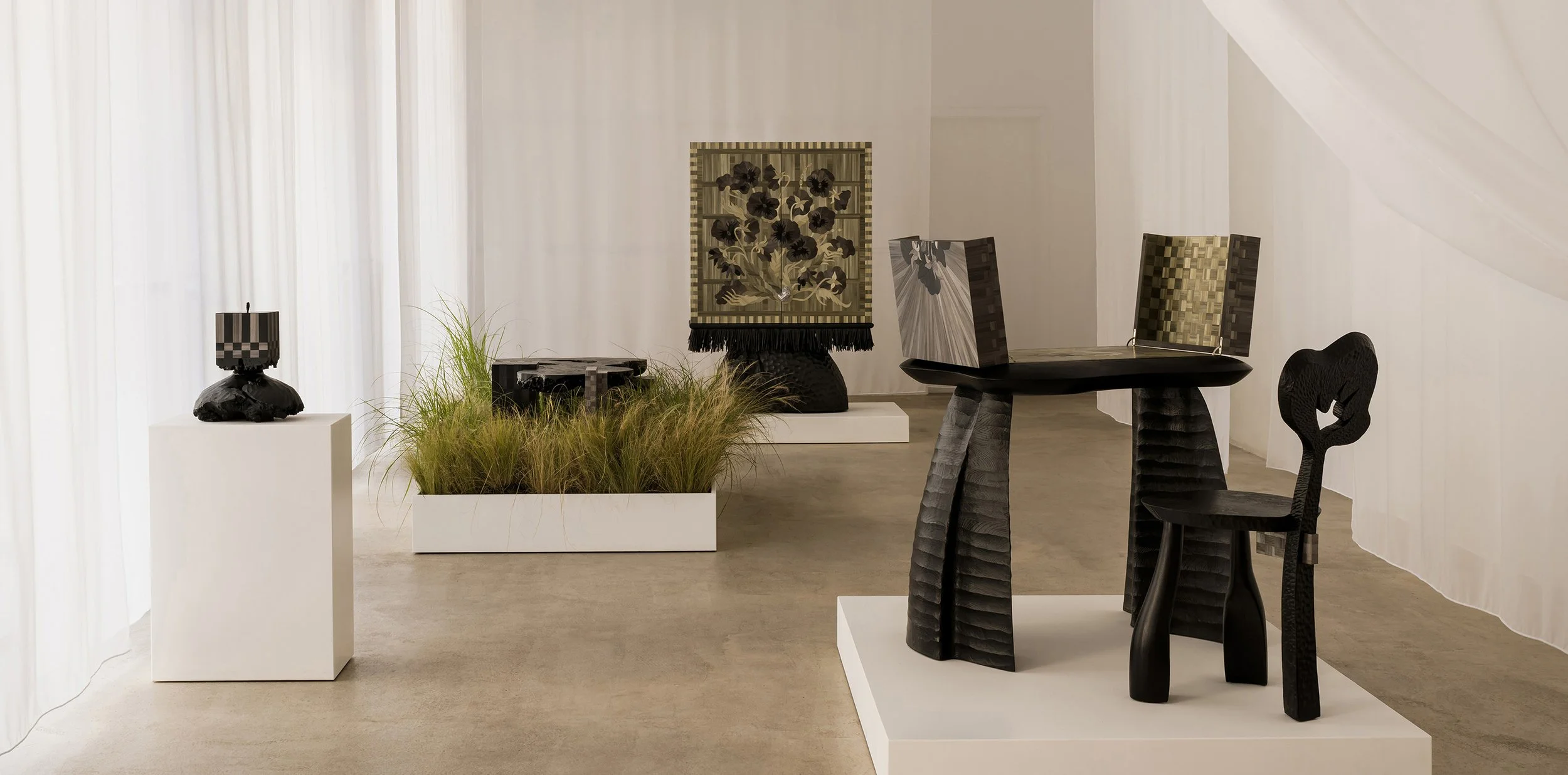 Art gallery with black sculptural furniture, decorative pieces, and textured artworks in a bright, minimalist setting.