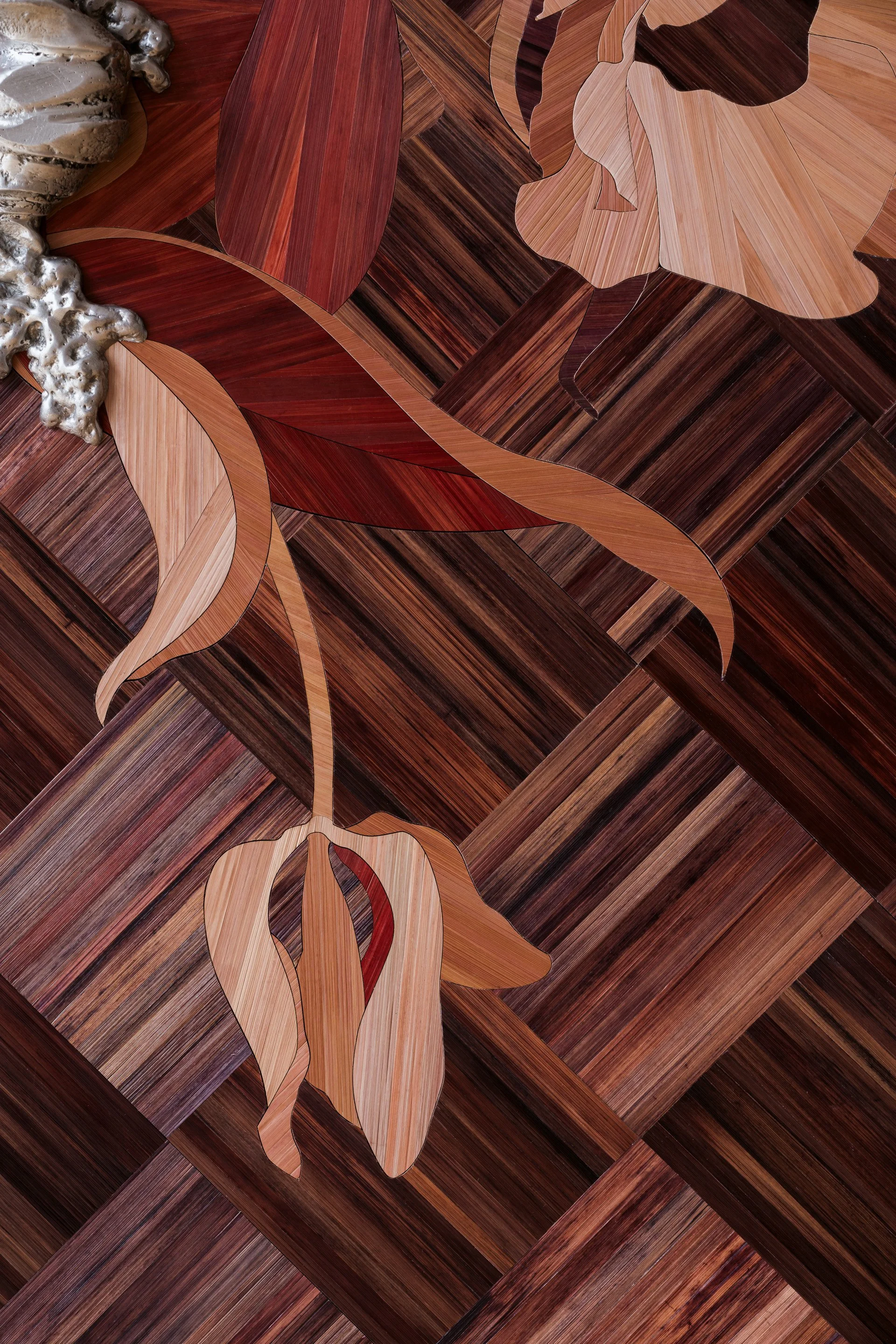 Close-up of an intricate inlaid wood parquet floor design featuring stylized flowers and leaves in various shades of wood.