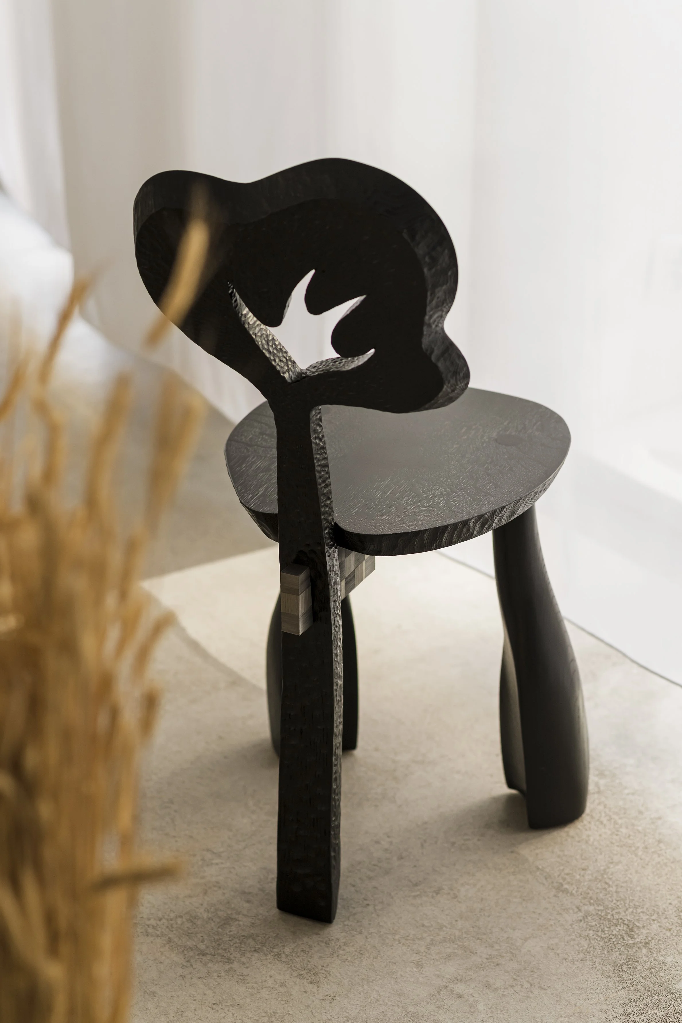 Black wooden chair with abstract, modern design placed on a beige carpet near a light-colored wall.