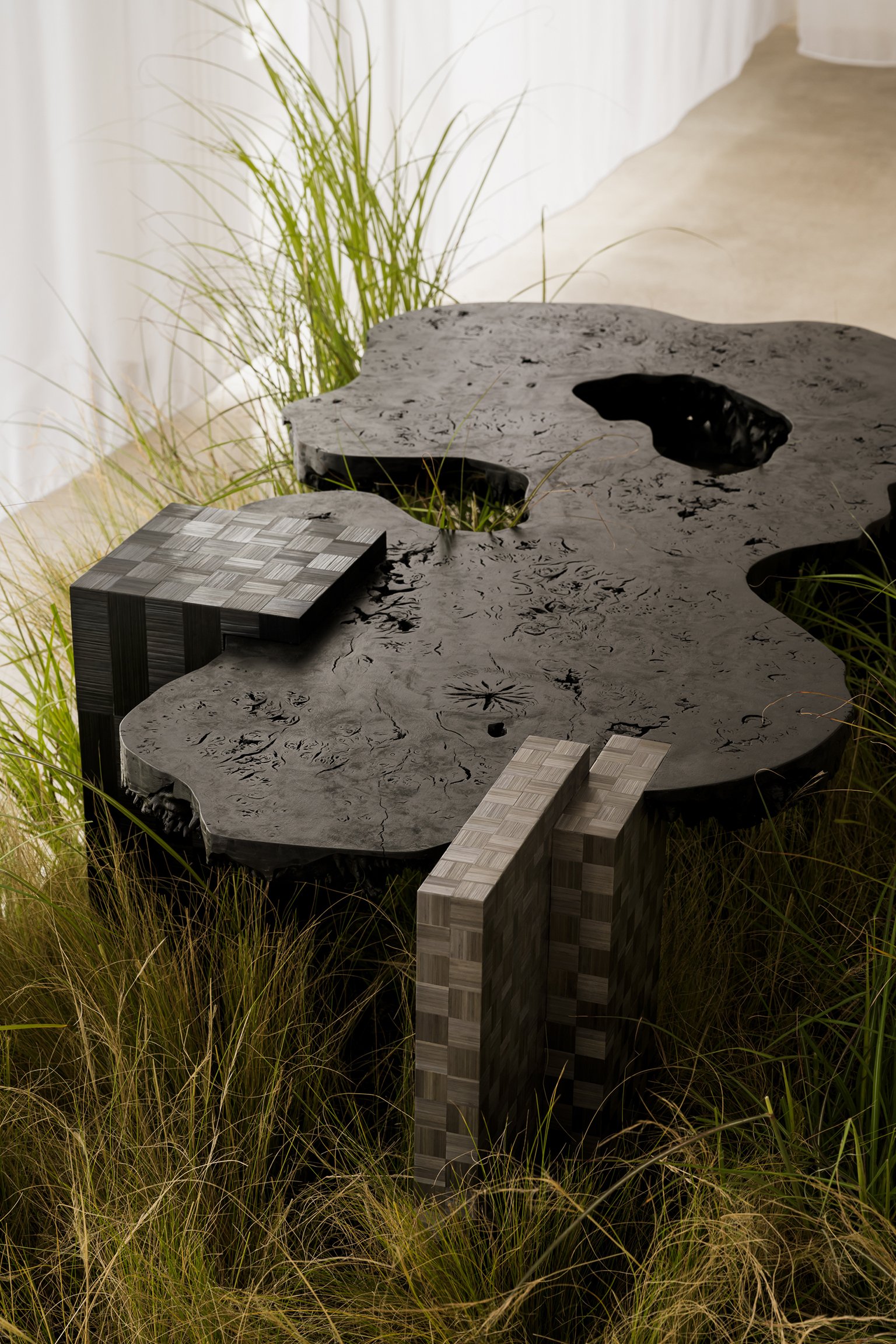 A unique table with a black, textured surface resembling a natural landscape, surrounded by green grass, with sections built from wooden blocks.
