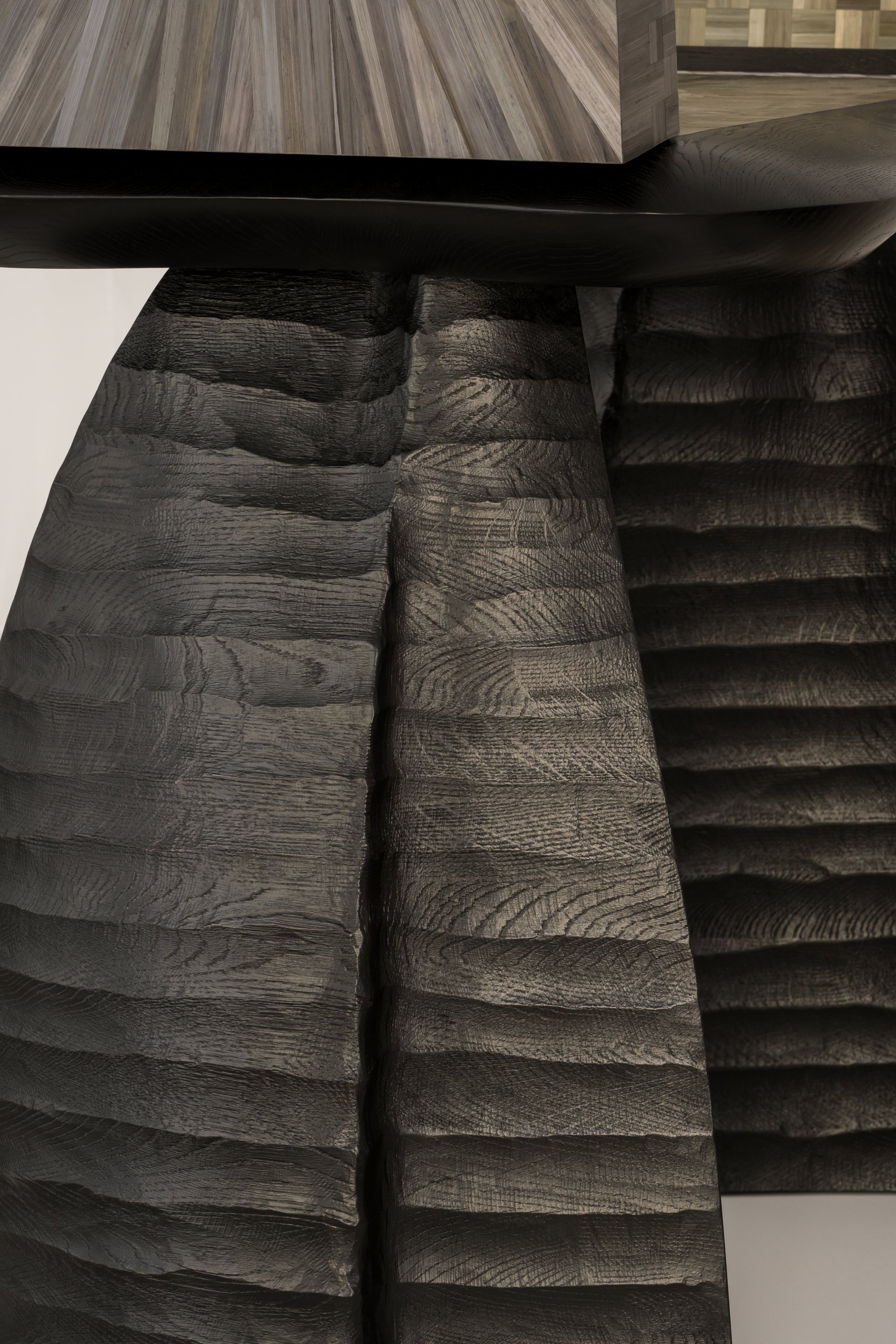 Close-up of stacked black wooden logs with textured grain patterns, supporting a wooden table with a light-colored, striped wooden surface.