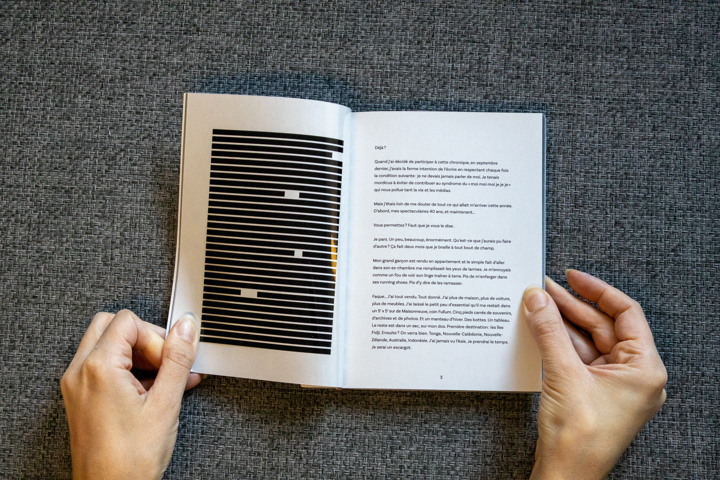 Un livre ouvert aux pages blanches et une illustration en bandes noires et blanches sur la page de gauche, posé sur une surface en tissu gris.
