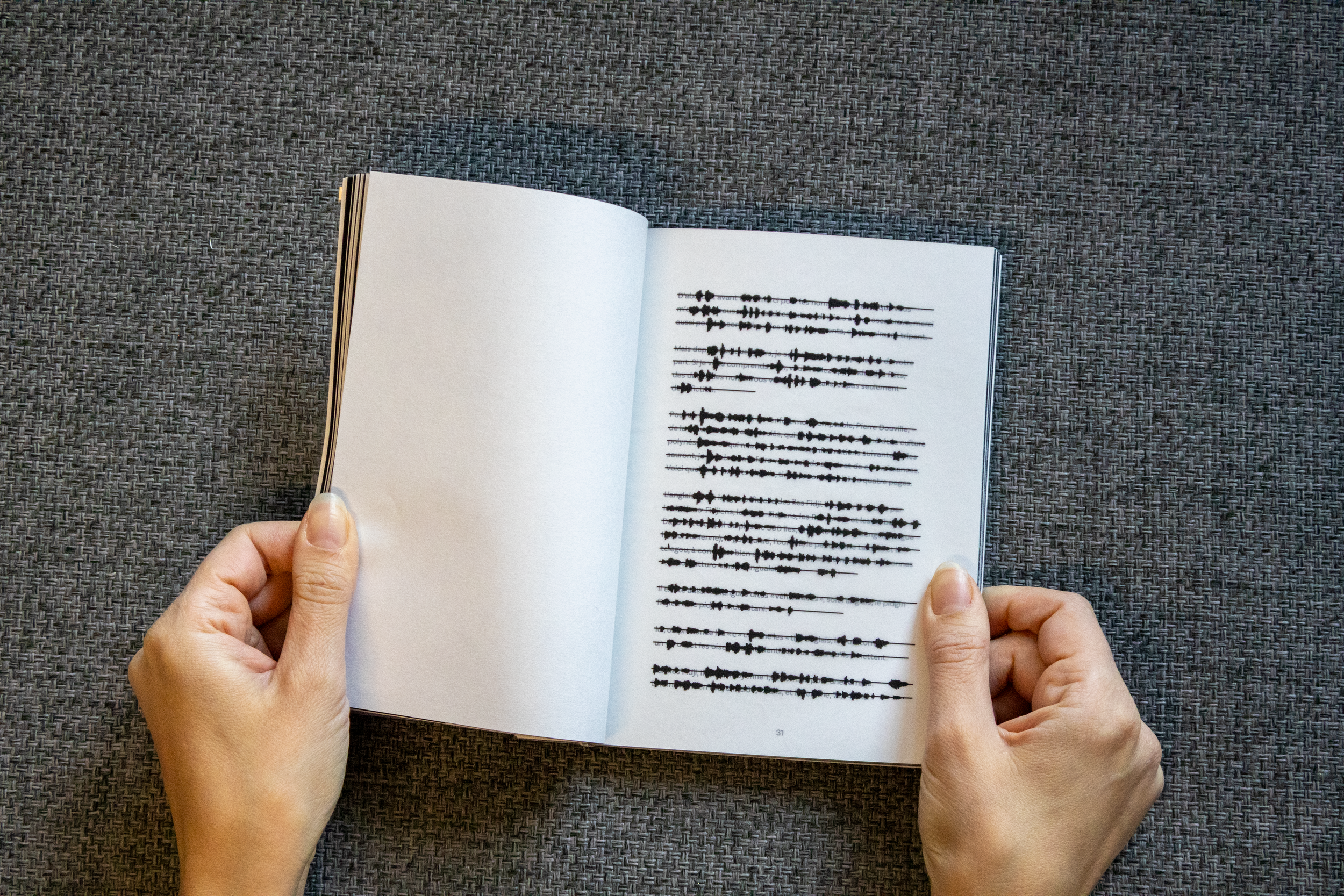 Une personne tient un livre ouvert montrant une image d'ondes sonores. Le livre est posé sur une surface en tissu gris.