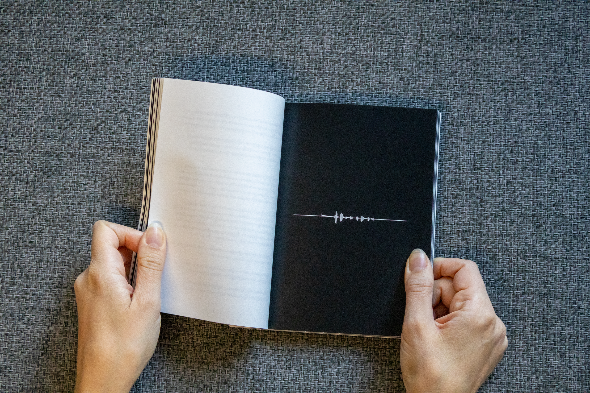 Une personne tient un livre ouvert avec une illustration de forme d'onde audio sur une page noire.