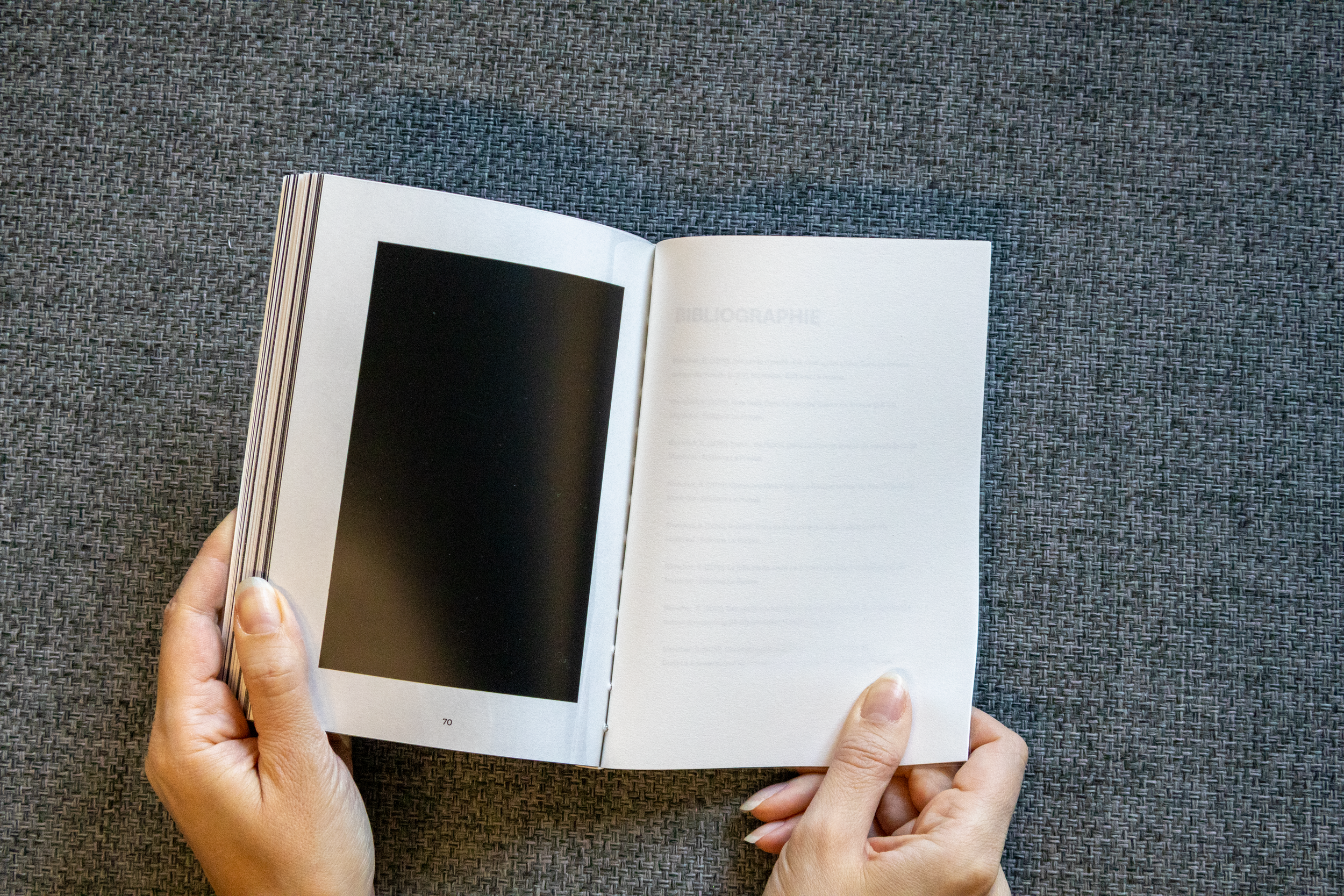 Une personne tenant un livre ouvert sur un fond en tissu gris.