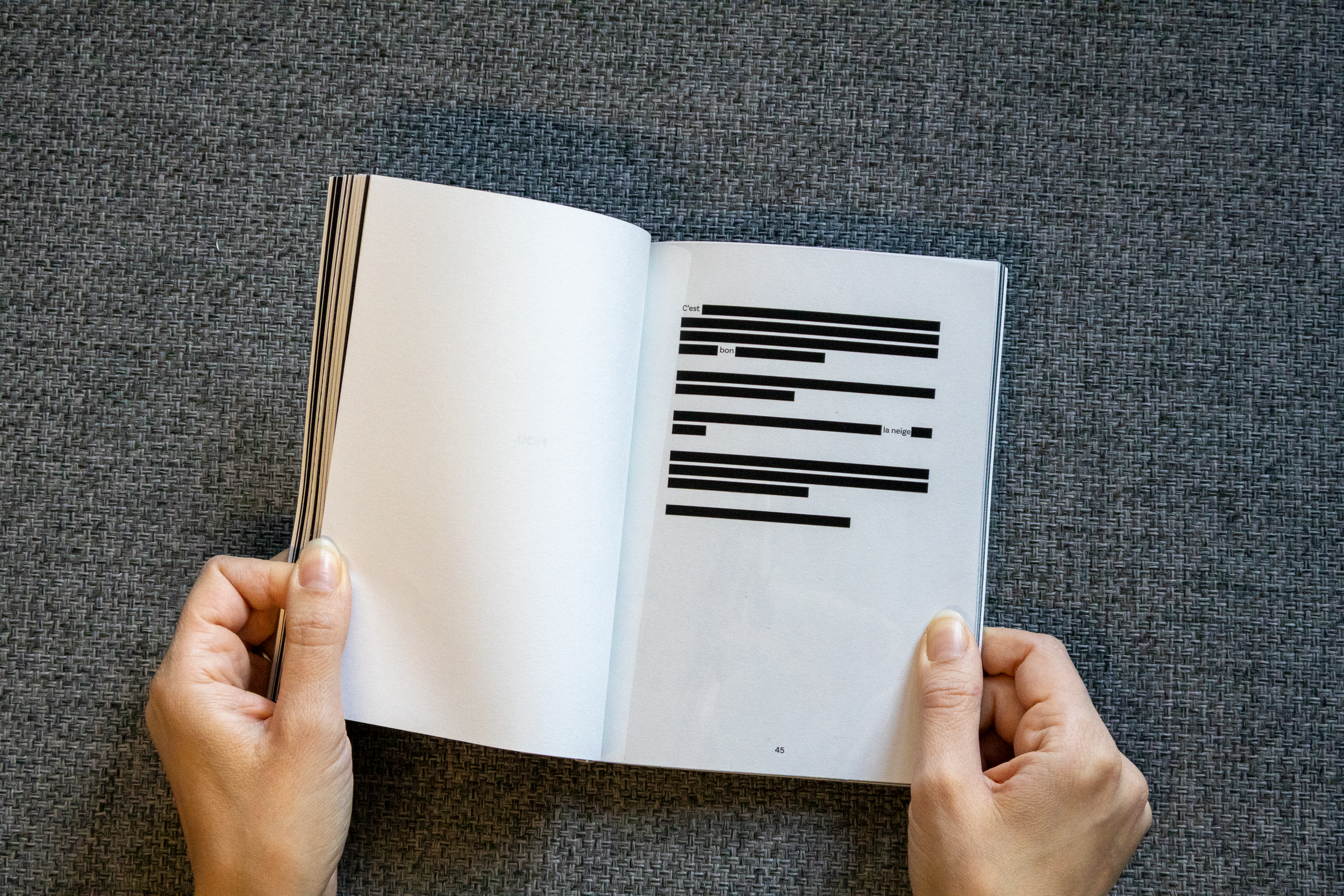 Un livre ouvert avec des lignes de texte noir barrées, posé sur une surface en tissu gris.