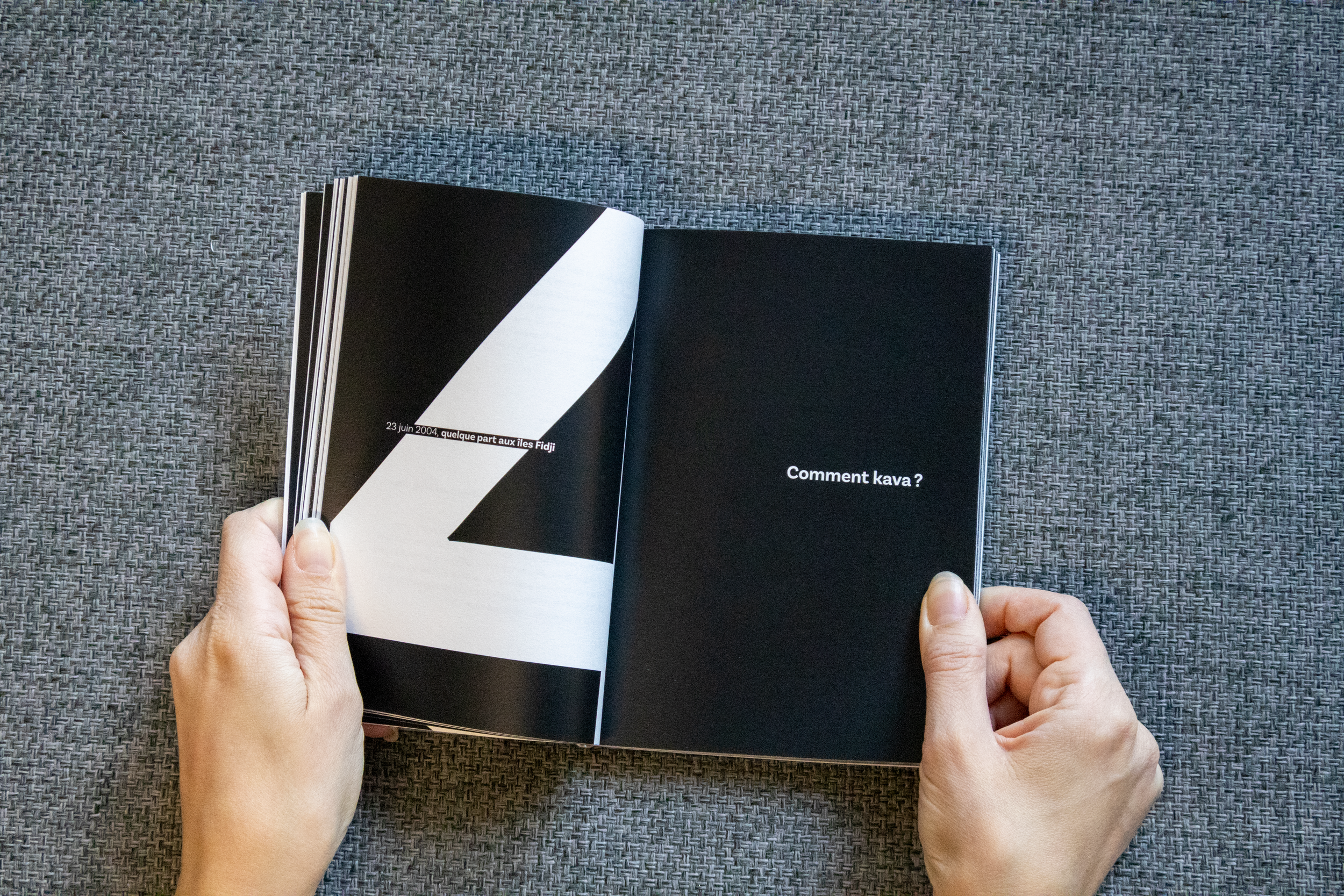 Une personne tient un livre ouvert avec une page noire et une phrase en français. La page de gauche a un motif géométrique noir et blanc tandis que la page de droite est noir avec une question en blanc : "Comment kava ?".