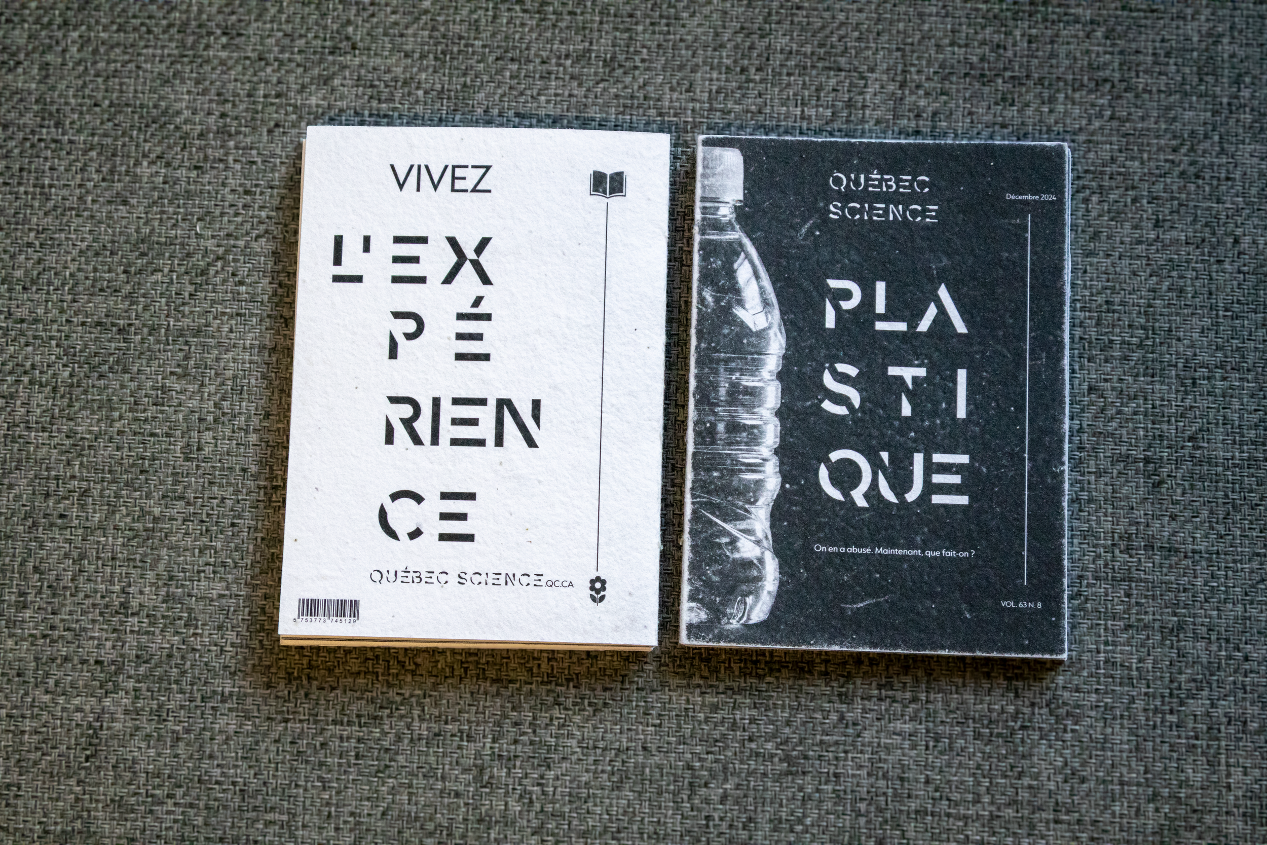 Deux magazines sur un fond gris aux textures diverses. L'un est blanc avec des textes en noir et un petit symbole d'une fleur à la base. L'autre est noir avec une photo de bouteille en plastique et des textes en blanc.