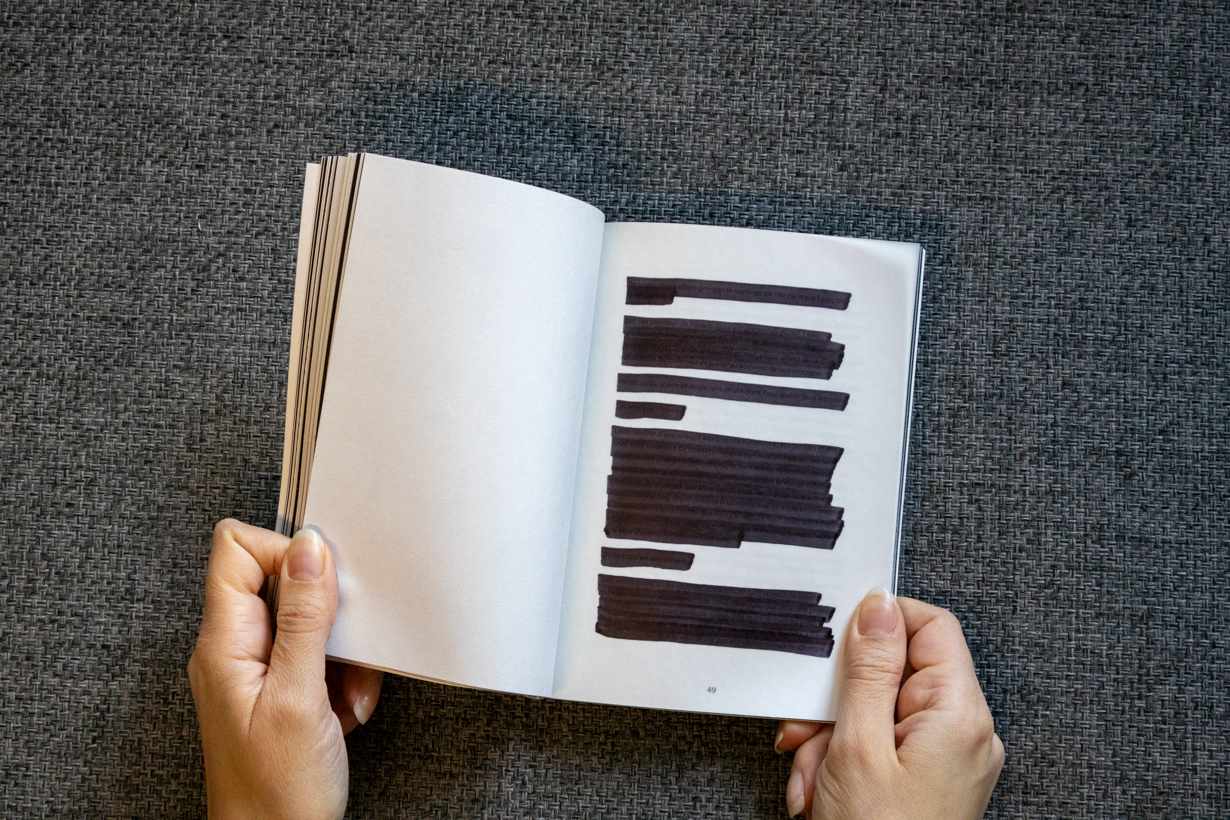 Main tenant un livre ouvert avec du texte noirage à l'intérieur, placé sur une surface en tissu sombre.