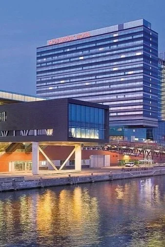 Mövenpick hotel aan het IJ bij avondlicht met verlichte gevel en weerspiegeling.
