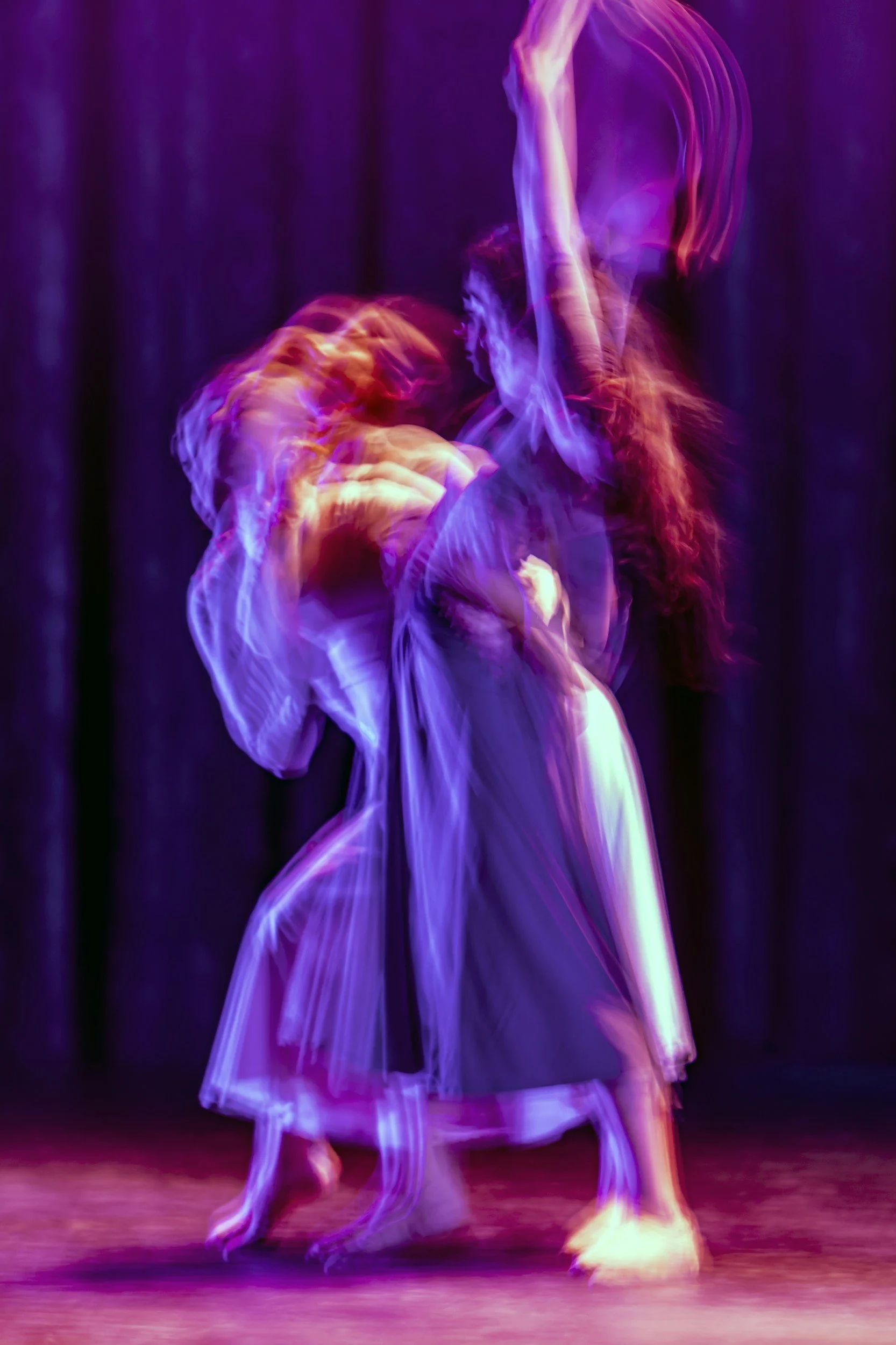 Twee dansers op een donkere achtergrond, bevroren in beweging door langexposure, onder kleurrijk stageverlichting.
